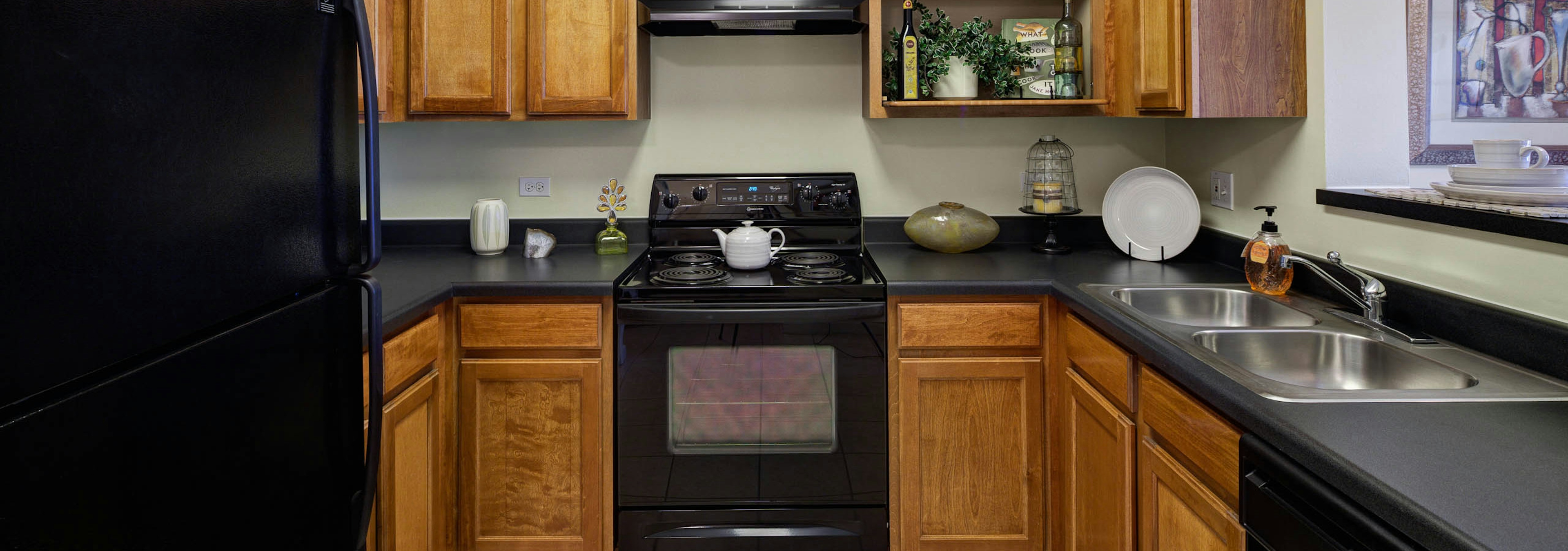 Interior view of kitchen at AMLI at Seven Bridges with black appliances and countertops paired with light brown wood cabinets