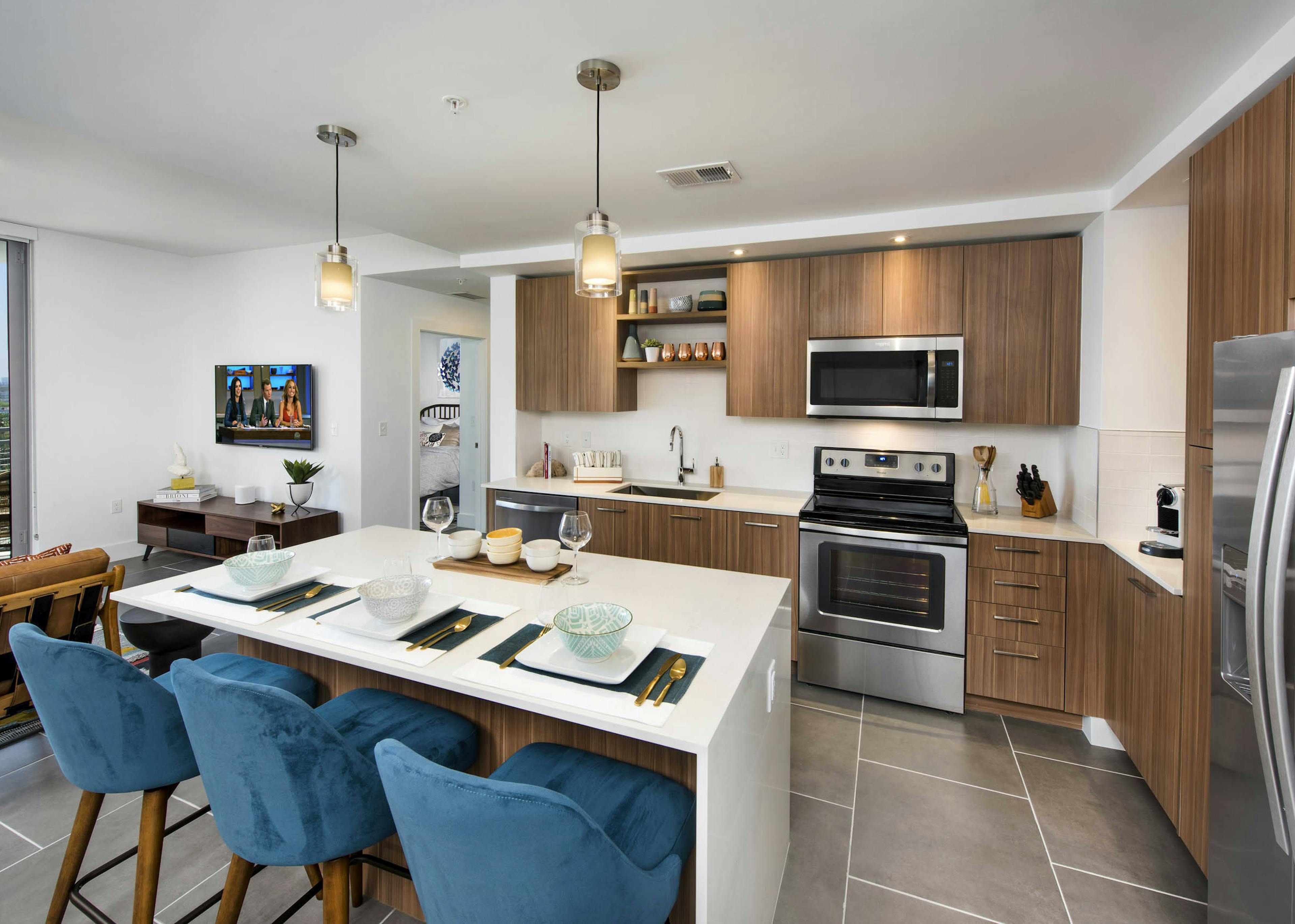 Interior kitchen with white island and blue chairs with pendant lighting and wood cabinets at AMLI Midtown 29 apartments