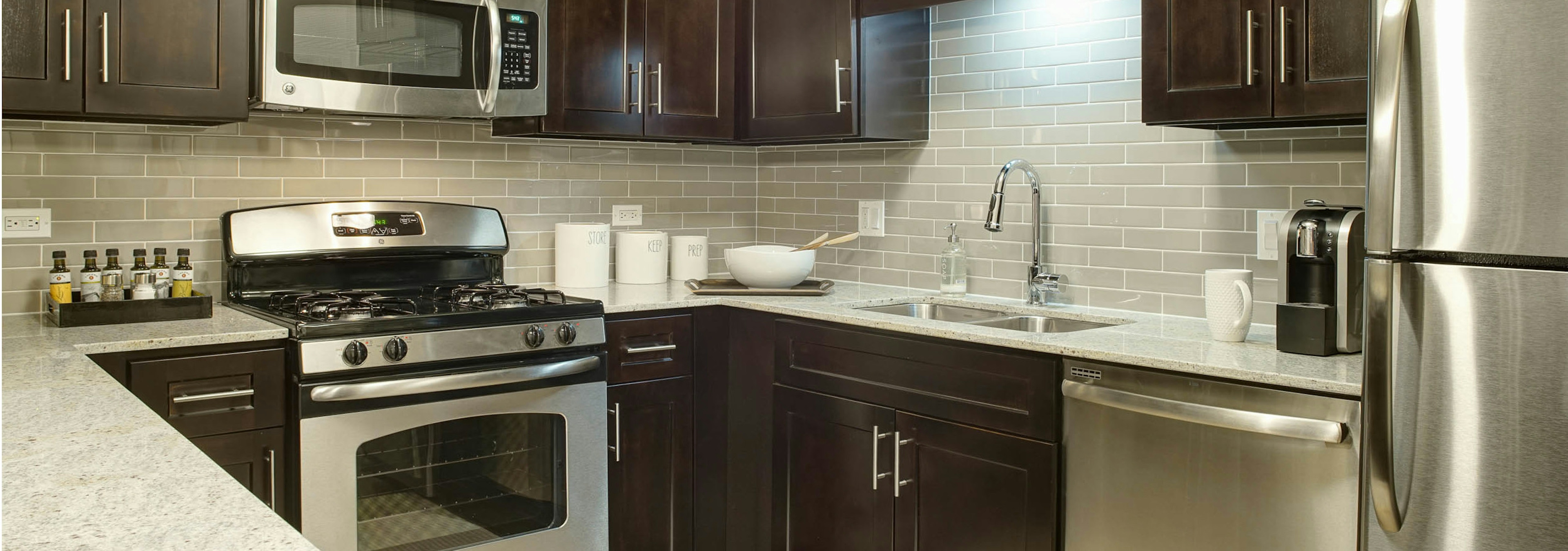 AMLI River North kitchen with dark cabinets and quartz countertops featuring stainless steel appliances and taupe backsplash