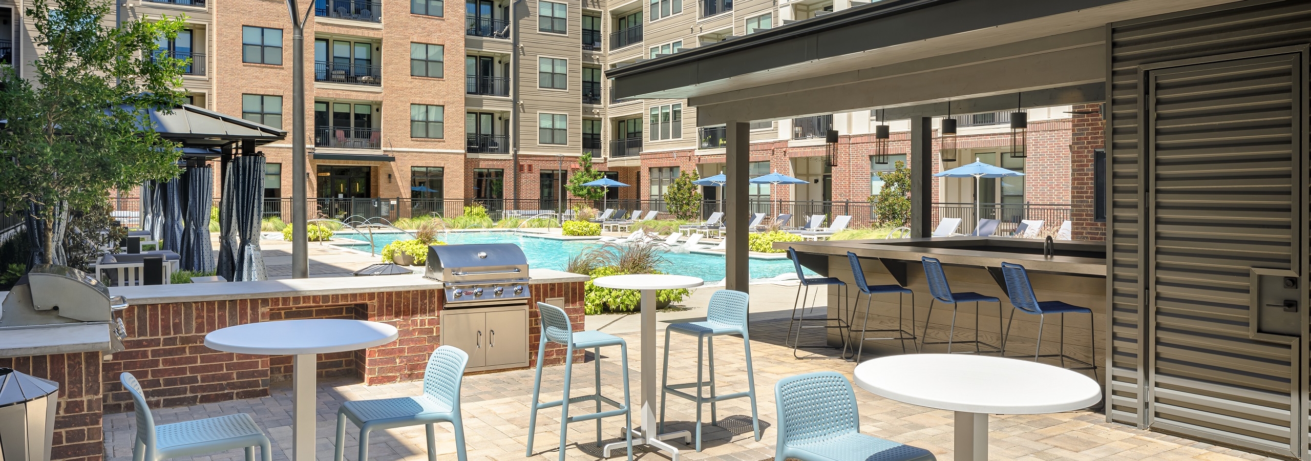 Grill station and 3 small tables with 2 chairs each in AMLI Addison courtyard with pool and cabanas and building in rear