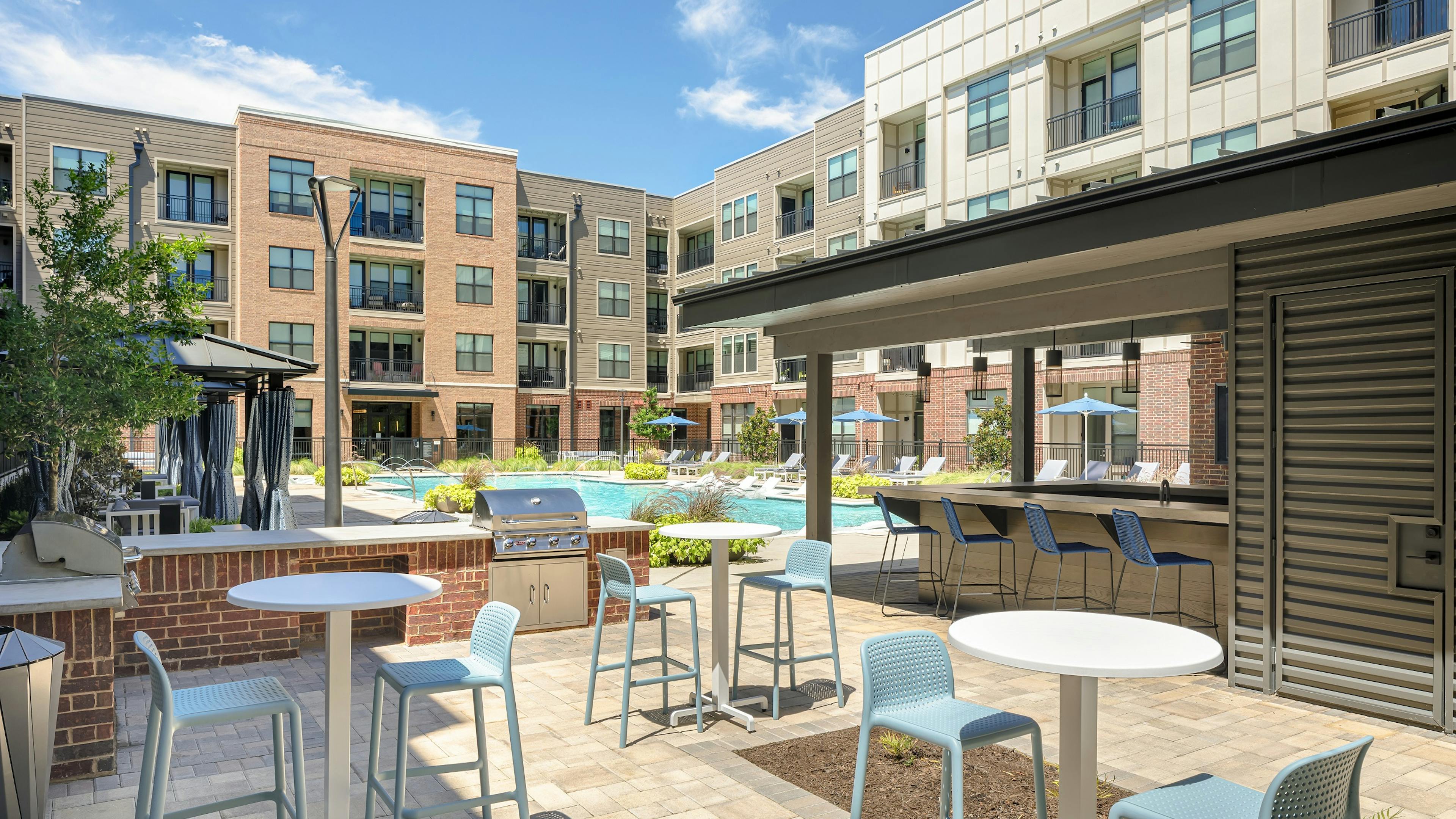 Grill station and 3 small tables with 2 chairs each in AMLI Addison courtyard with pool and cabanas and building in rear
