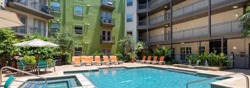 Daytime AMLI 300 resort-style swimming pool surrounded by greenery and with orange outdoor lounge seating