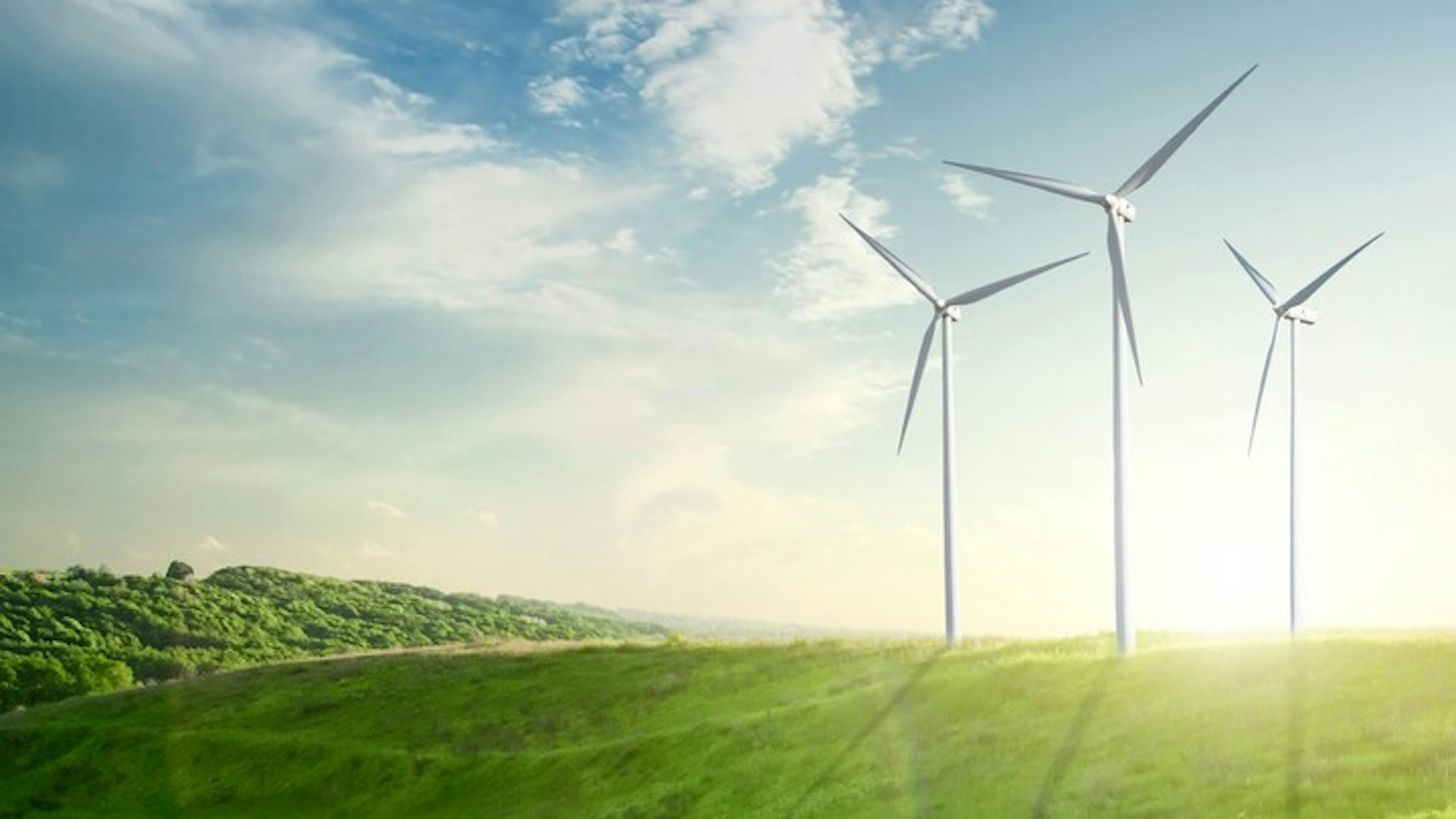 Three white windmills on a hill of vibrant green grass with a bright golden sun setting in the sky behind them