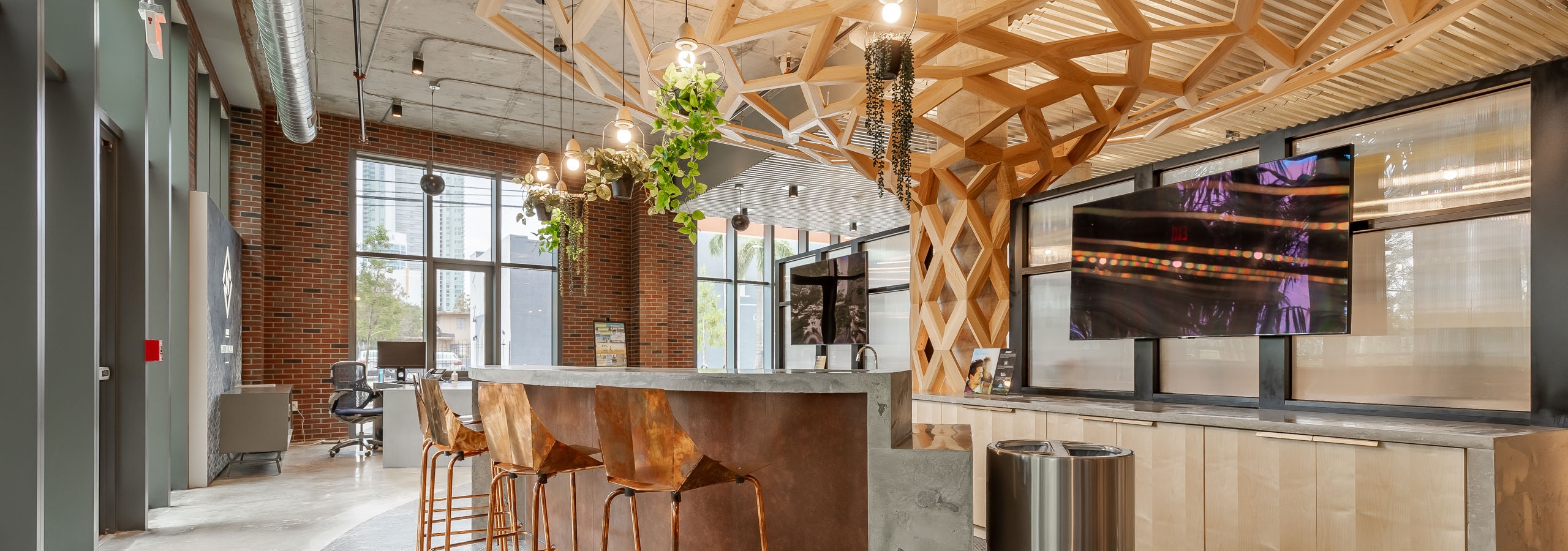 AMLI Midtown Miami leasing office with tall counter and copper stools and hanging plant fixtures with a wood sculpture above