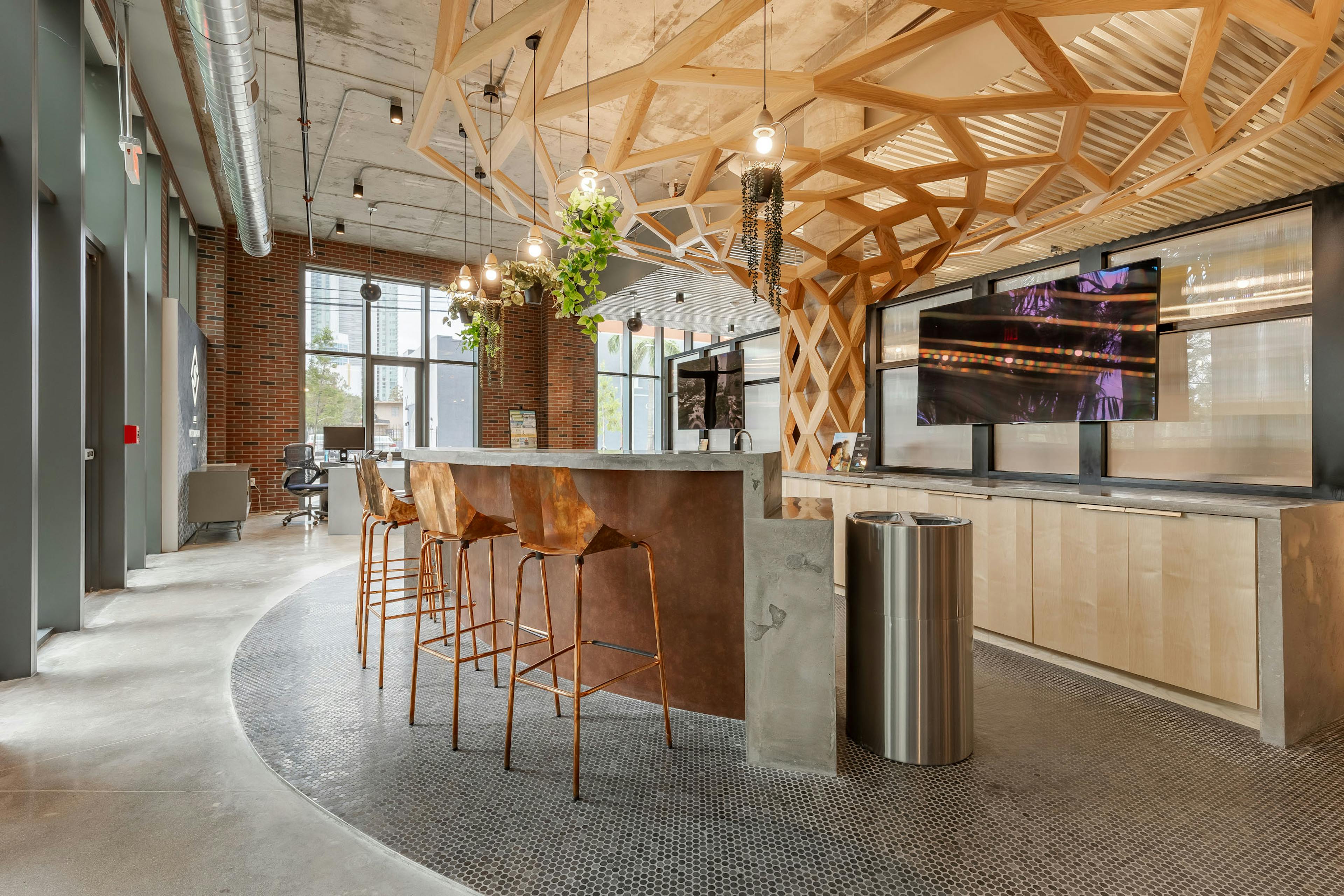 AMLI Midtown Miami leasing office with tall counter and copper stools and hanging plant fixtures with a wood sculpture above 