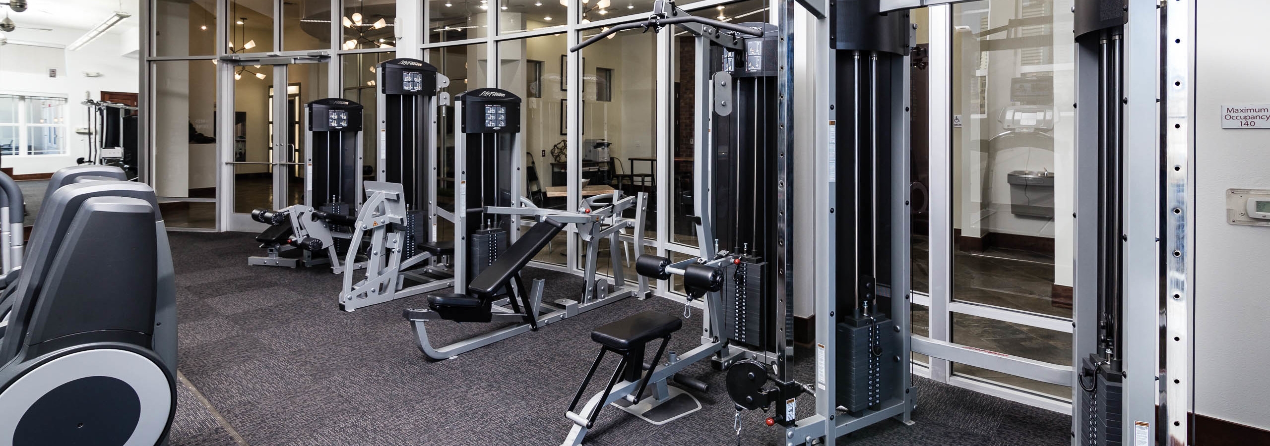 View of the fitness center at AMLI Park Avenue apartments with free weights and other strength training machines with windows
