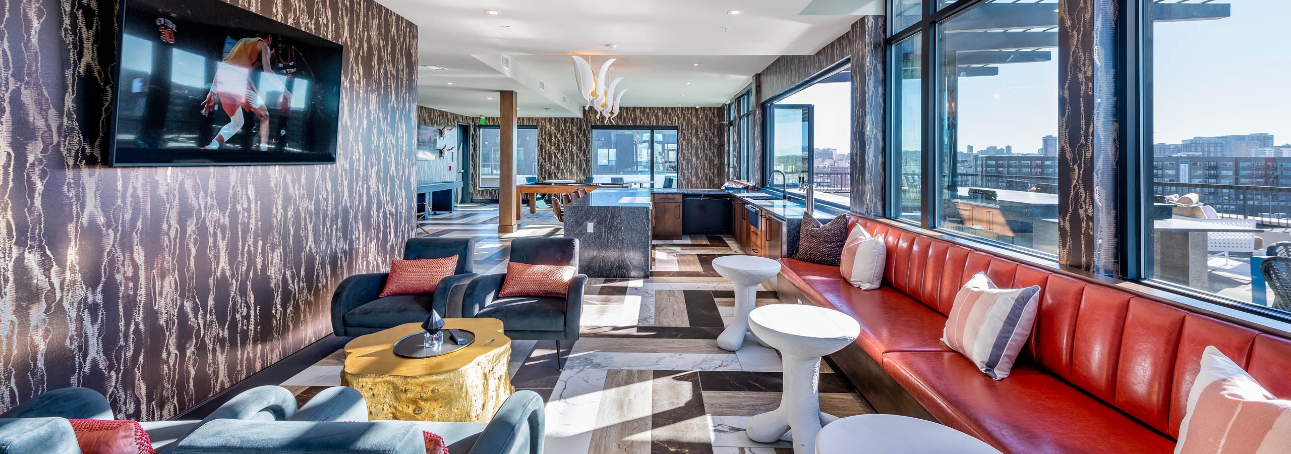 AMLI Art District resident sky lounge with vibrant chairs and tables with a television and view of bar and downtown Denver