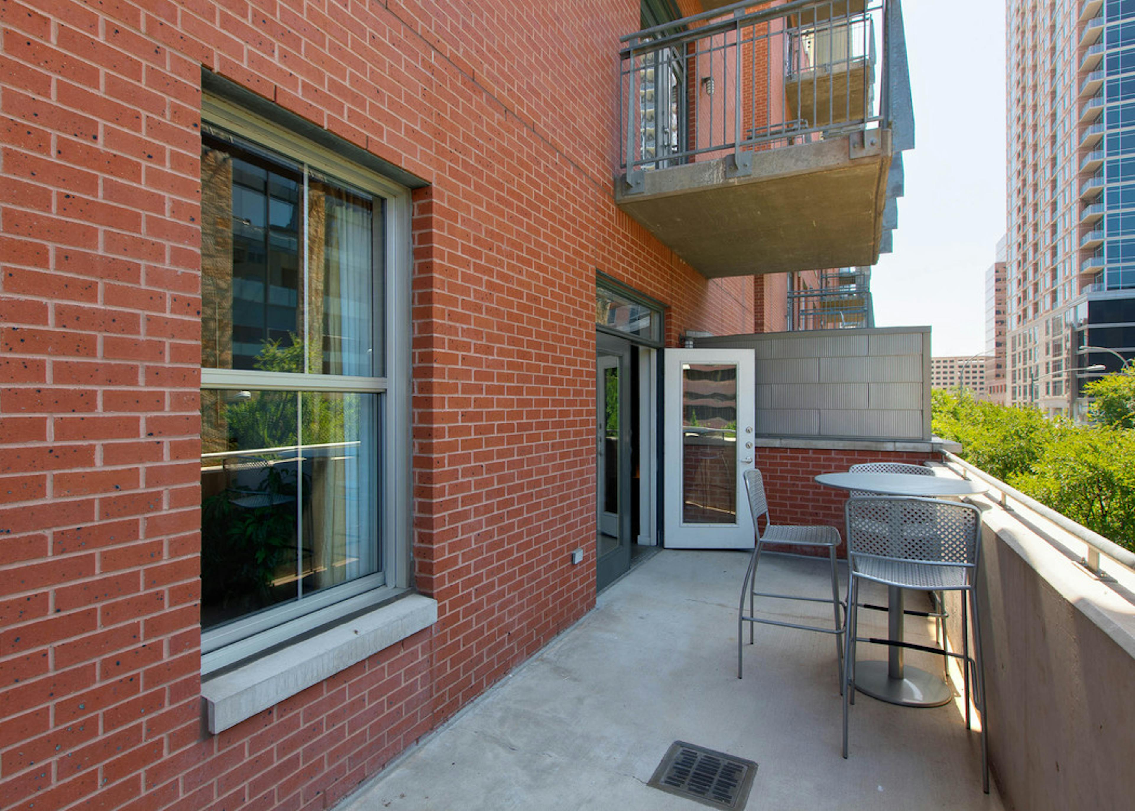 View of oversized balcony at AMLI Downtown with red brick façade and silver tables and chairs and window on the left 