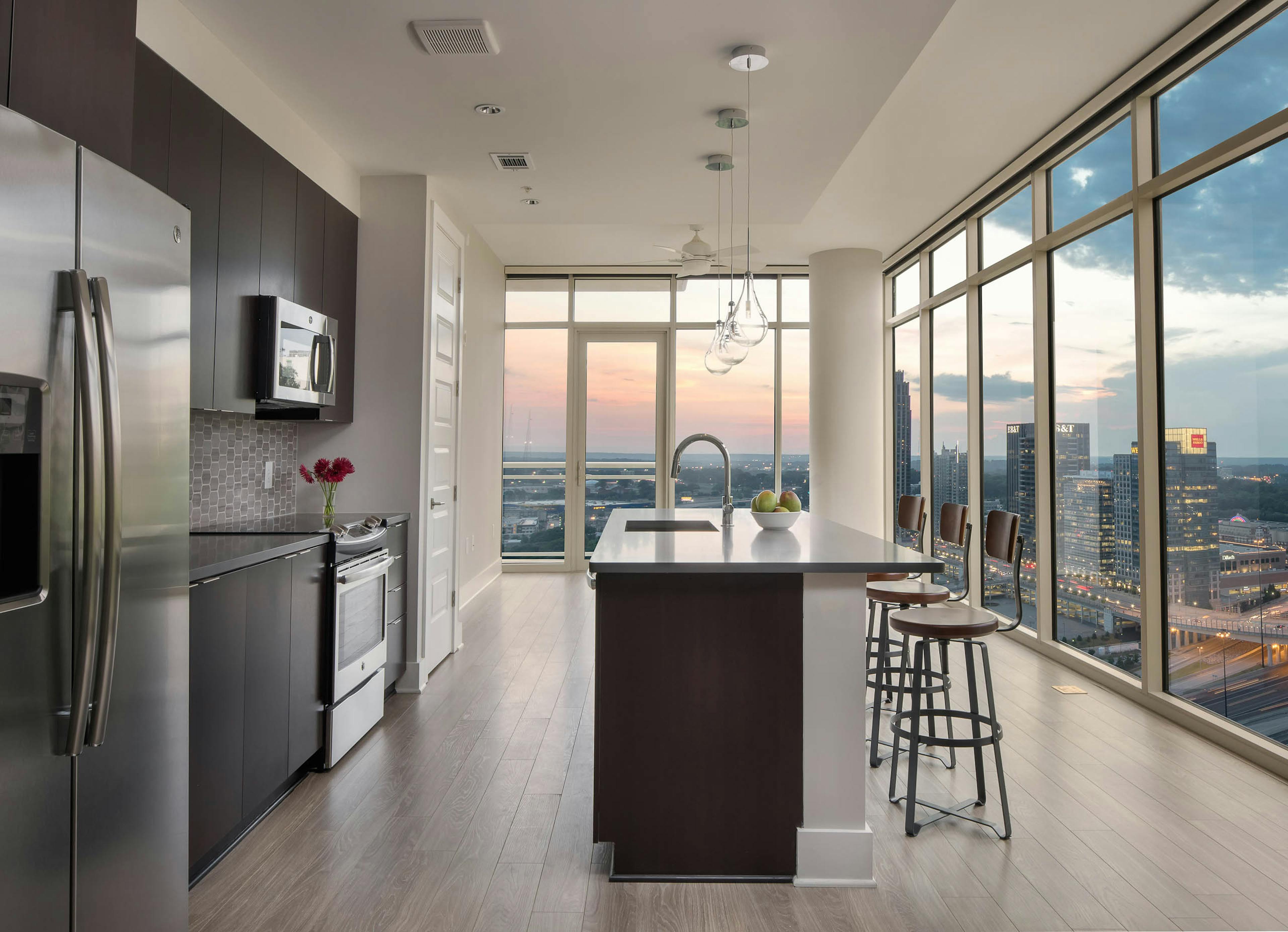 Kitchen at AMLI Arts Center with floor to ceiling windows showing a sunset city view with an island and industrial barstools