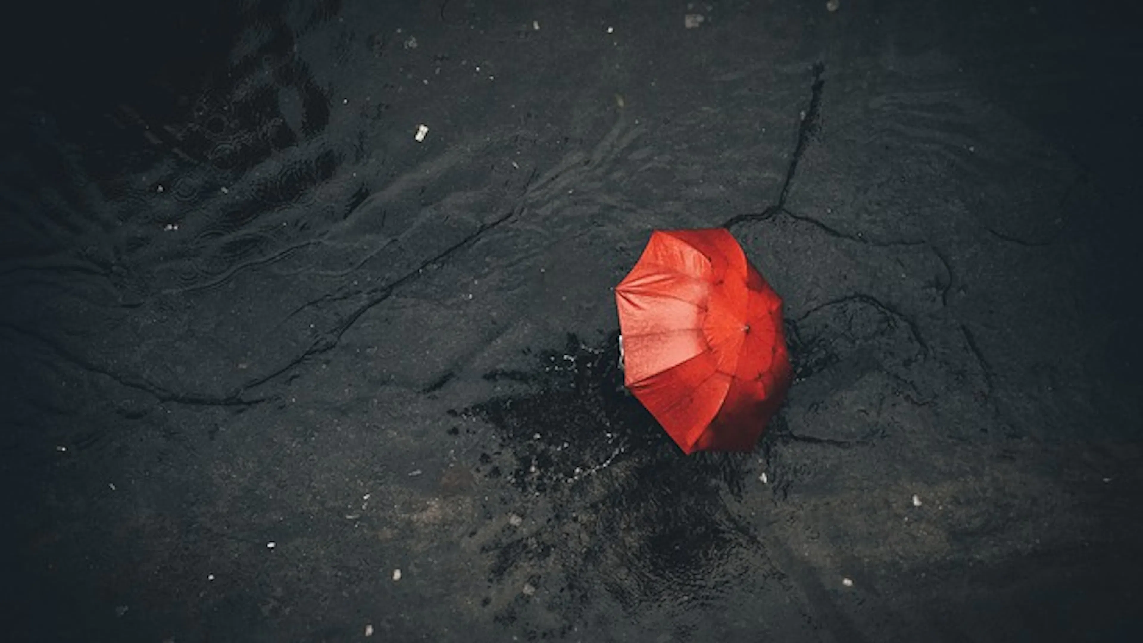 A person holding a red umbrella viewed from above on a rainy asphalt road