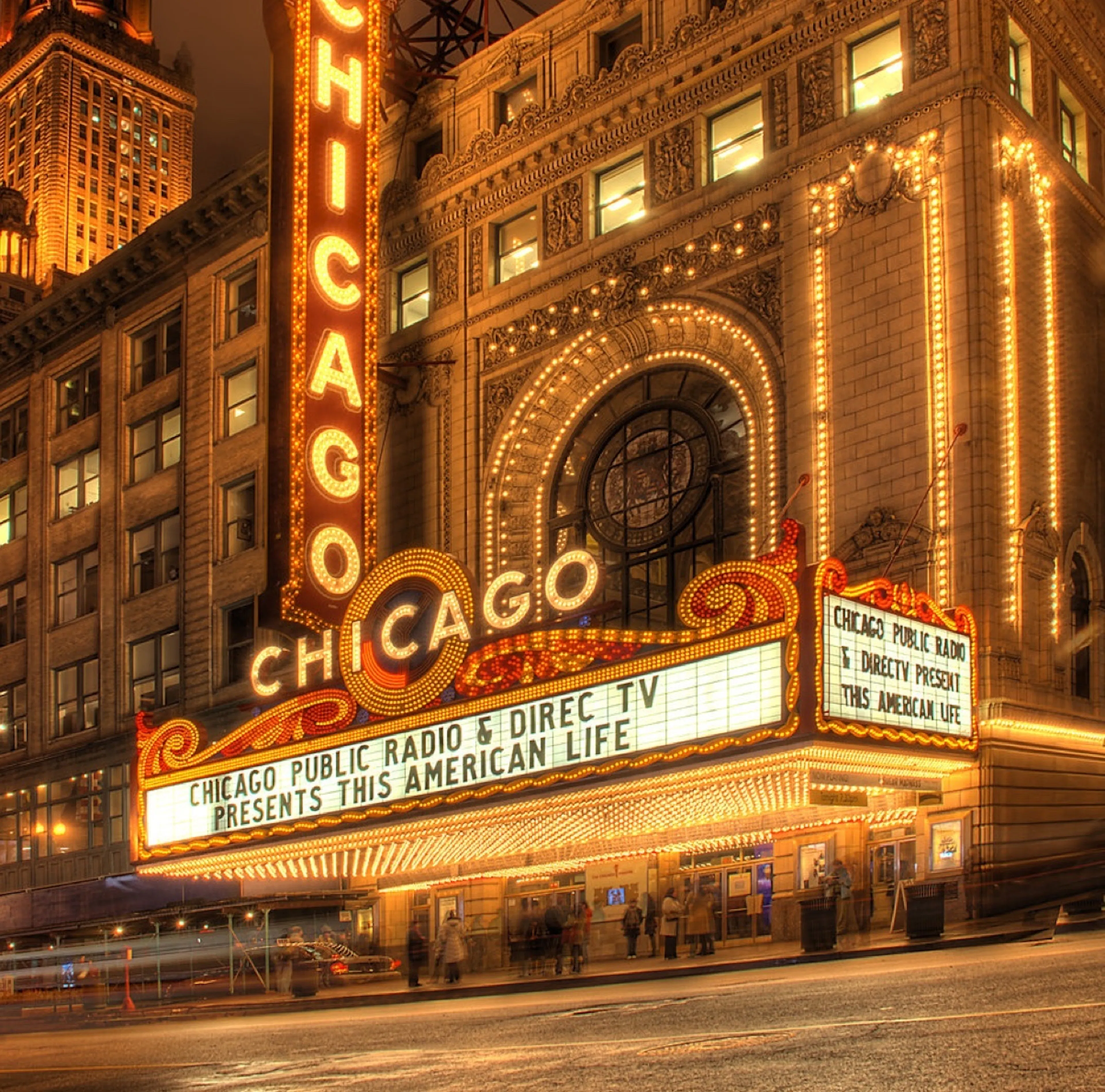 Exterior view of the Chicago Theatre lit up at night with the marquee displaying a show for This American Life