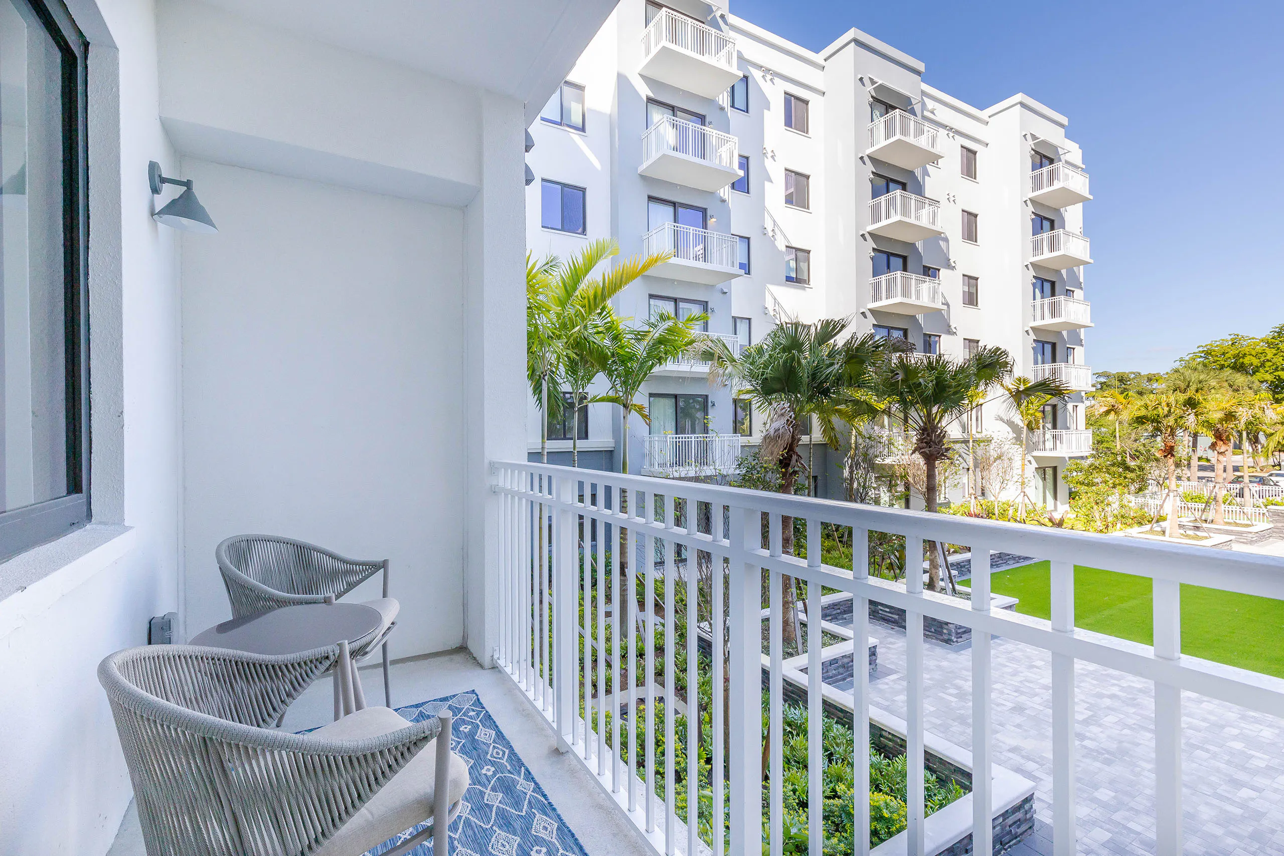 Exterior view of AMLI Park West apartment balcony with white metal bars and gray table and 2 chairs and a view of courtyard