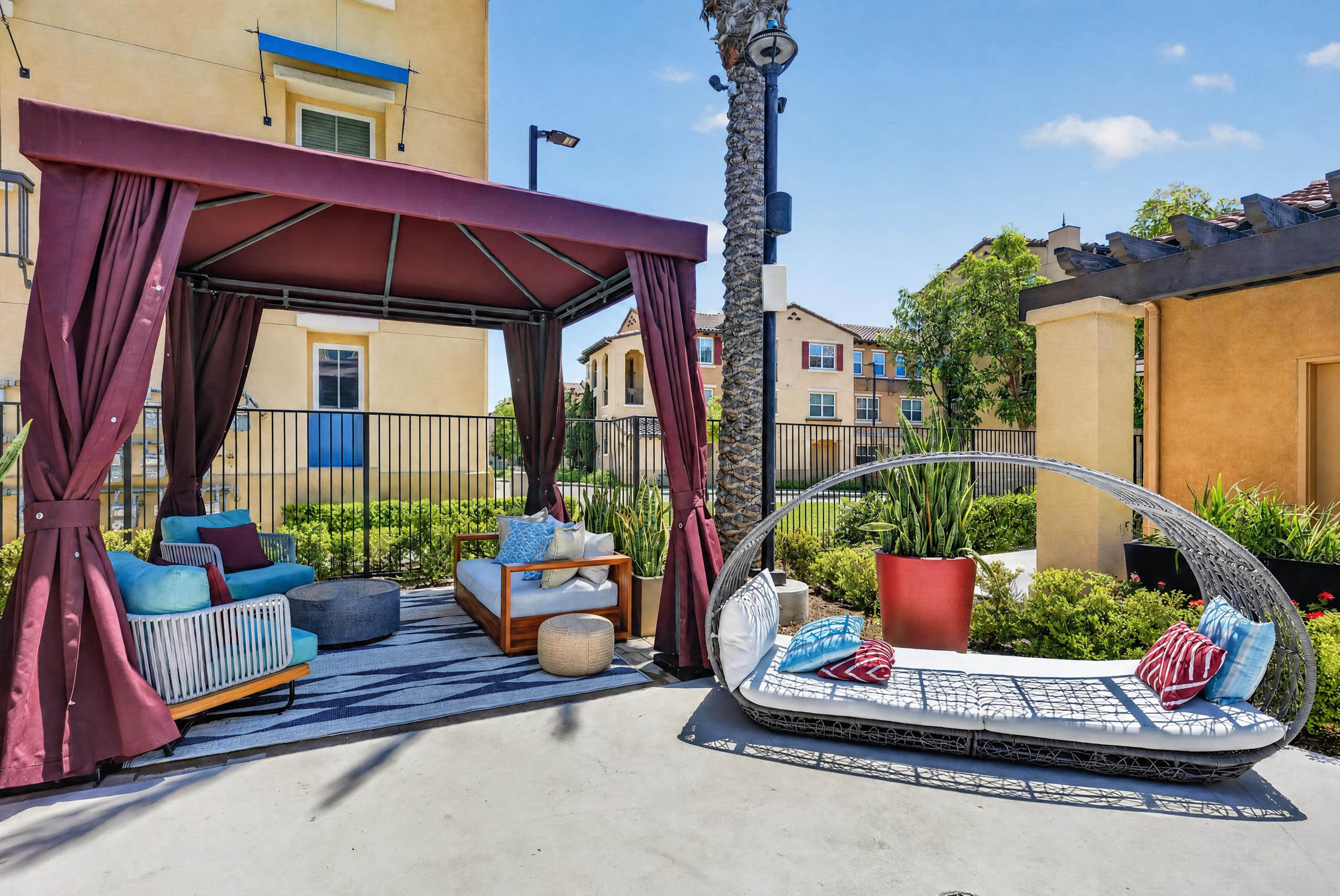 Poolside shaded cabana lounge seating at AMLI Camarillo apartments with cushioned daybed, palm tree and landscaped courtyard.