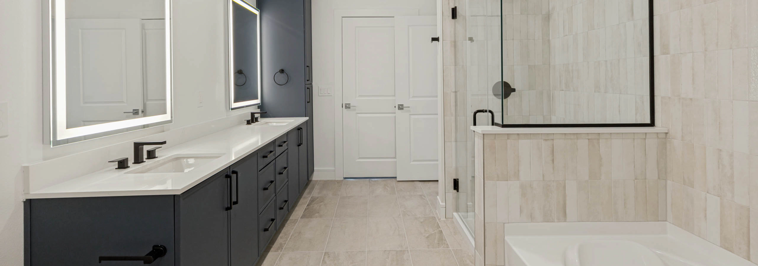 Beautifual bathroom with double vanity, illuminated mirrors, quartz countertops, glass-enclosed shower, soaking tub, and tile flooring.
