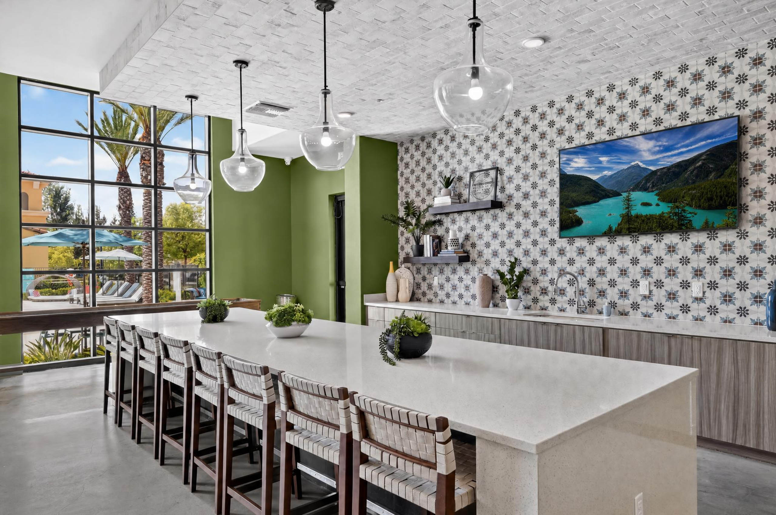 Bright AMLI Camarillo apartments clubhouse kitchen with large island, bar seating, pendant lights and patterned tile backsplash.