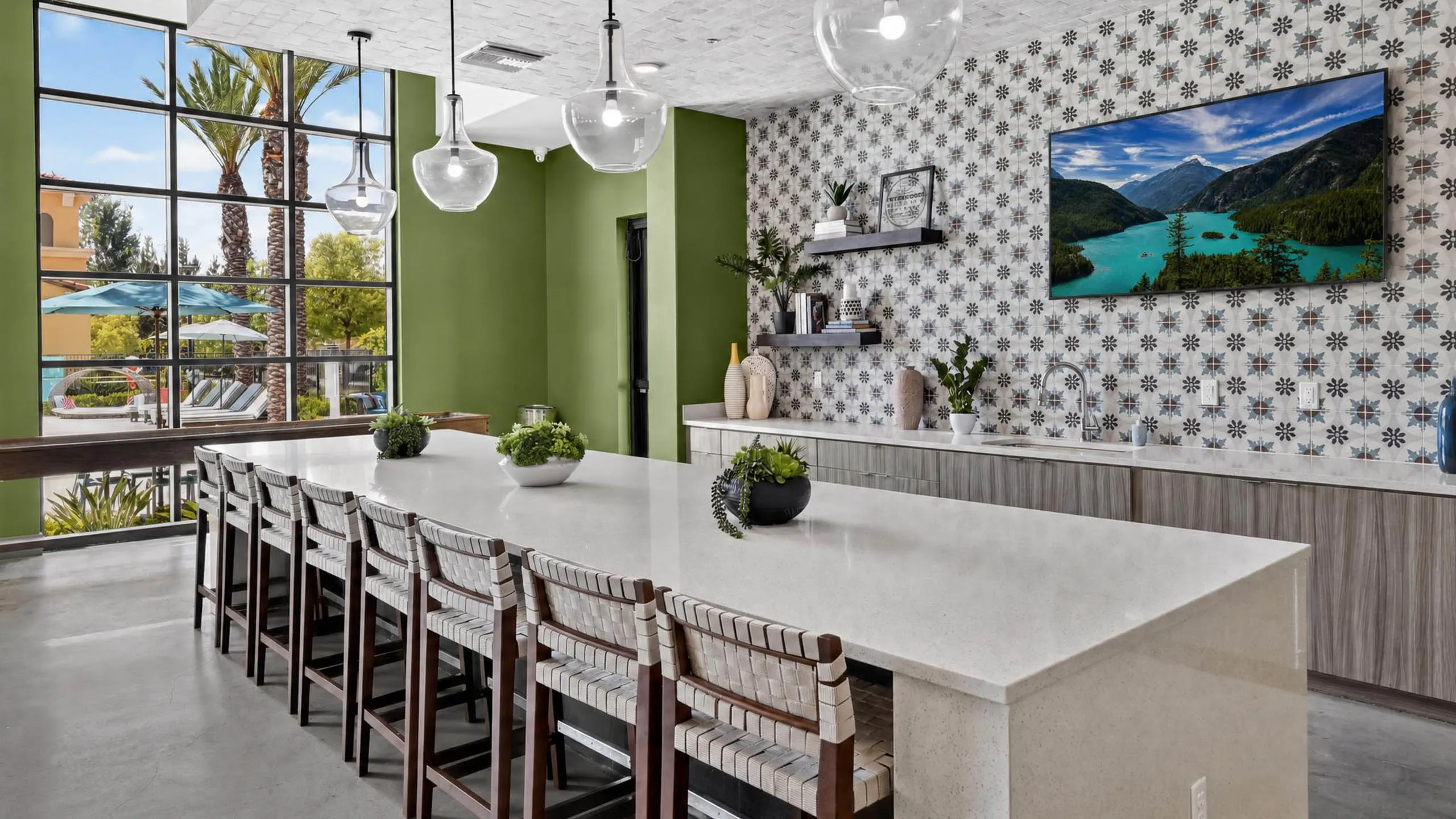 Bright AMLI Camarillo apartments clubhouse kitchen with large island, bar seating, pendant lights and patterned tile backsplash.