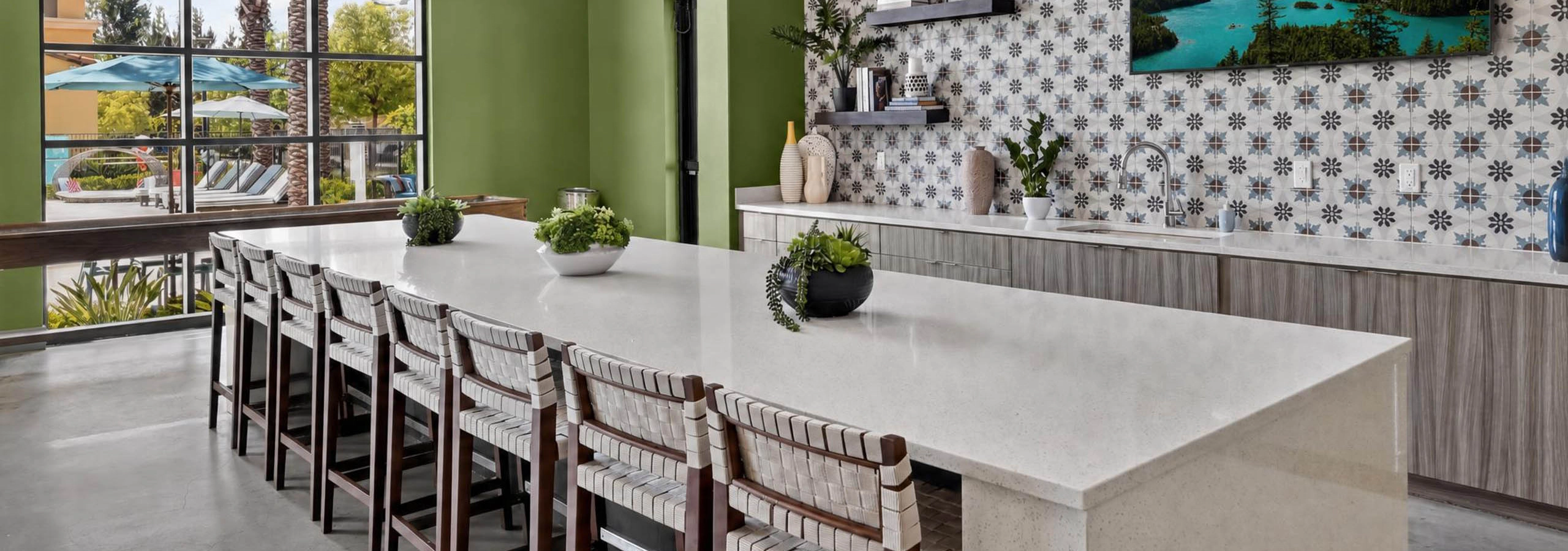 Bright AMLI Camarillo apartments clubhouse kitchen with large island, bar seating, pendant lights and patterned tile backsplash.