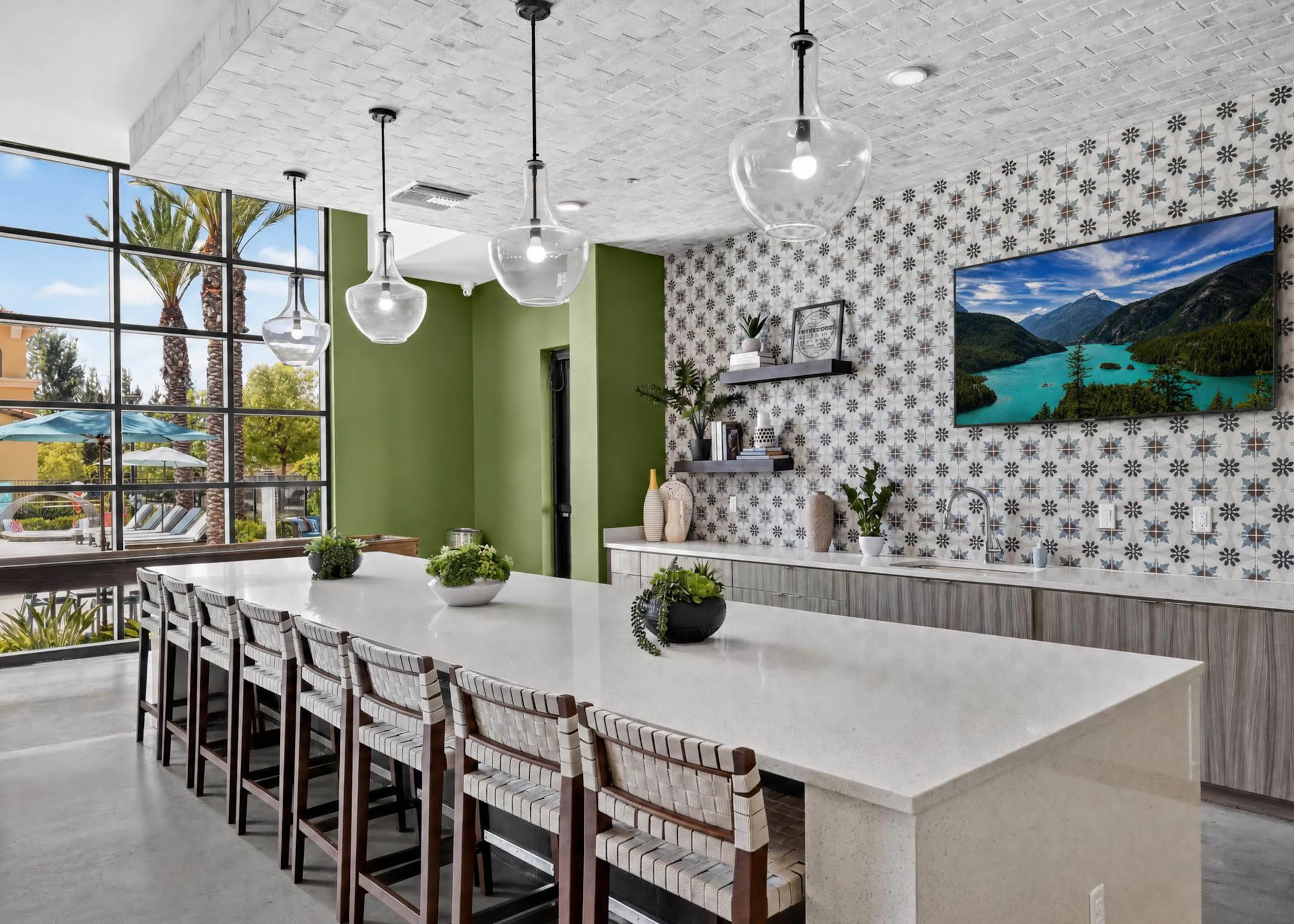 Bright AMLI Camarillo apartments clubhouse kitchen with large island, bar seating, pendant lights and patterned tile backsplash.