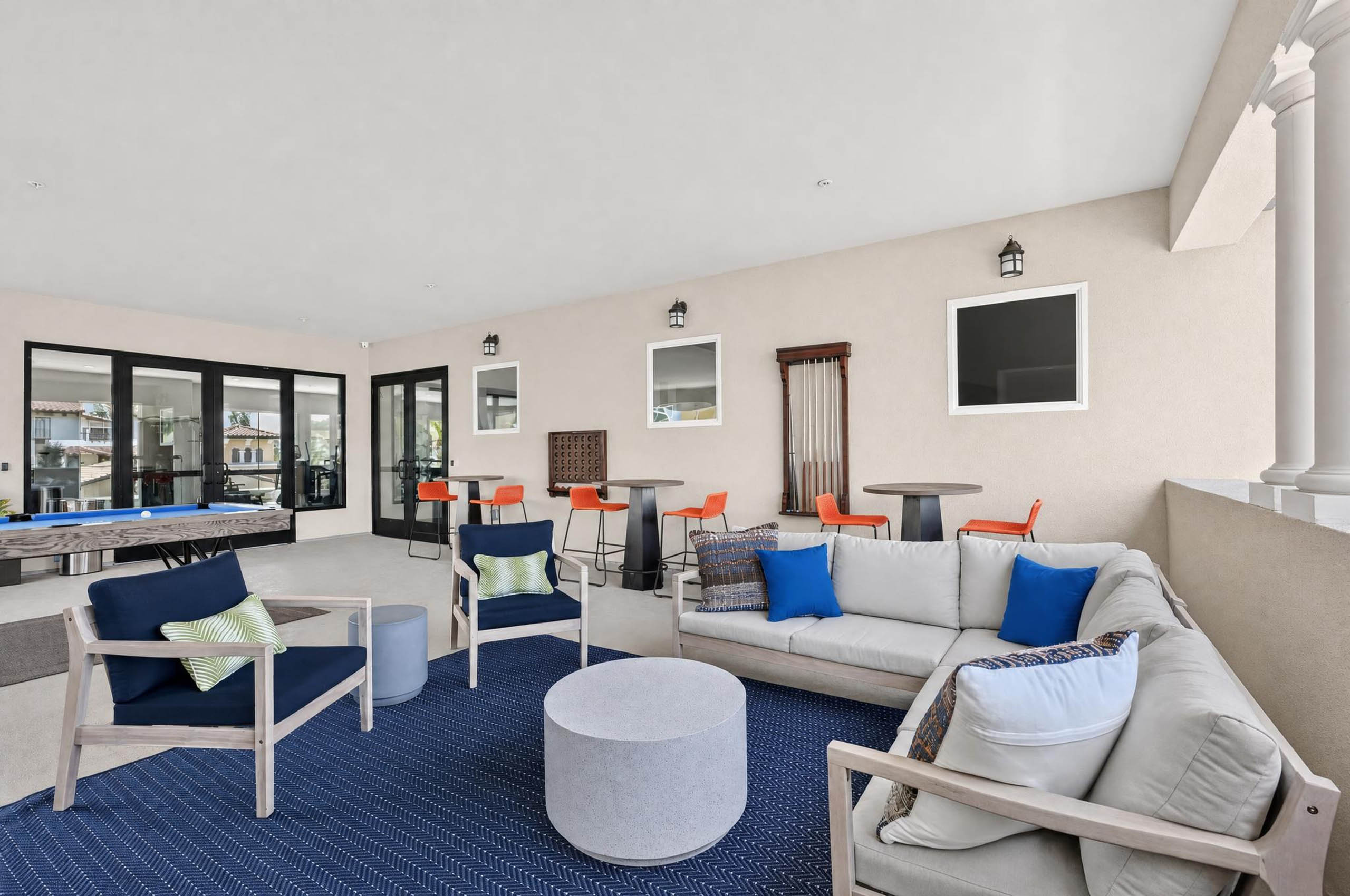 Covered game lounge at AMLI Camarillo apartments with cushioned seating, blue rug, billiards table and high top tables.