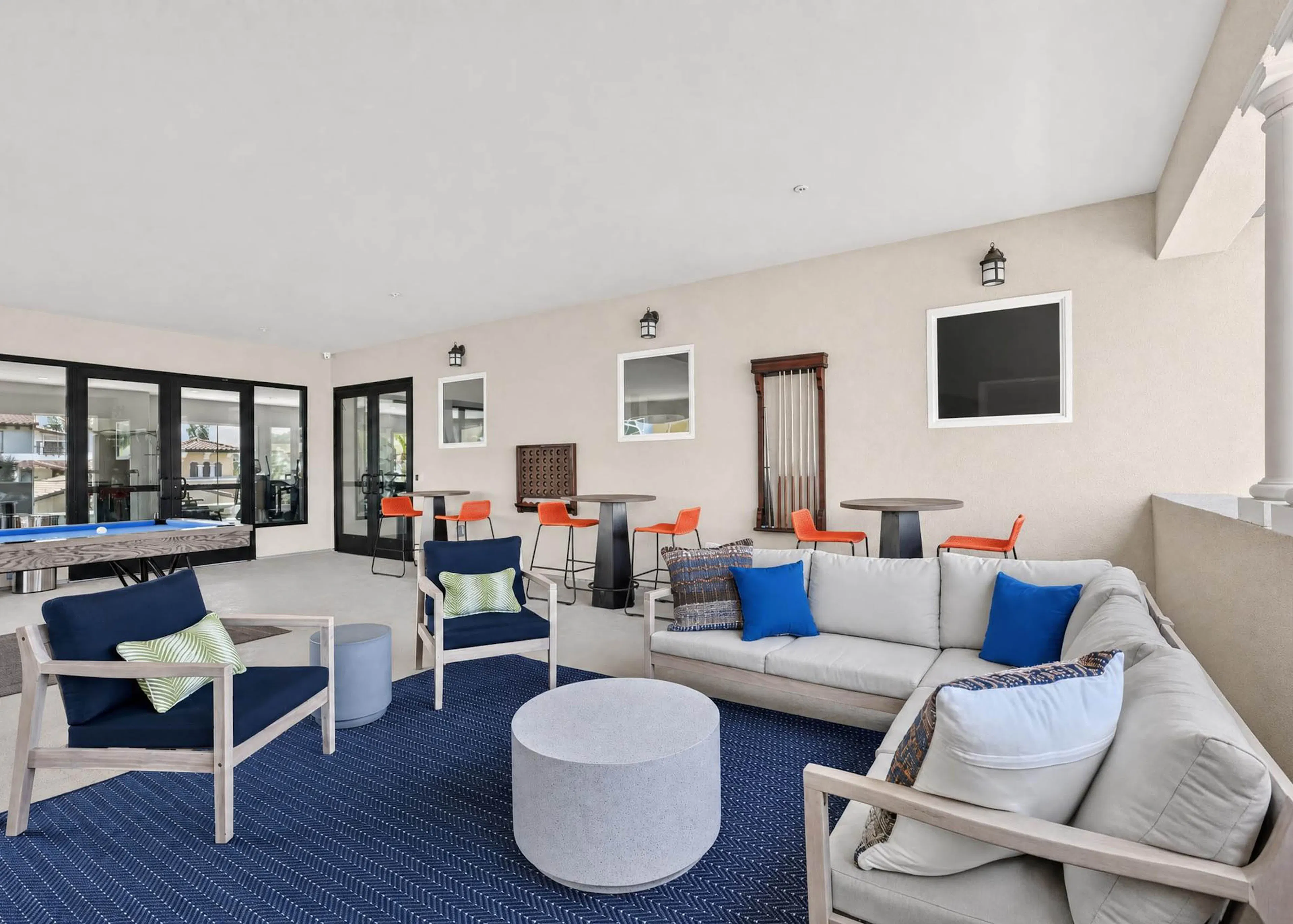 Covered game lounge at AMLI Camarillo apartments with cushioned seating, blue rug, billiards table and high top tables.