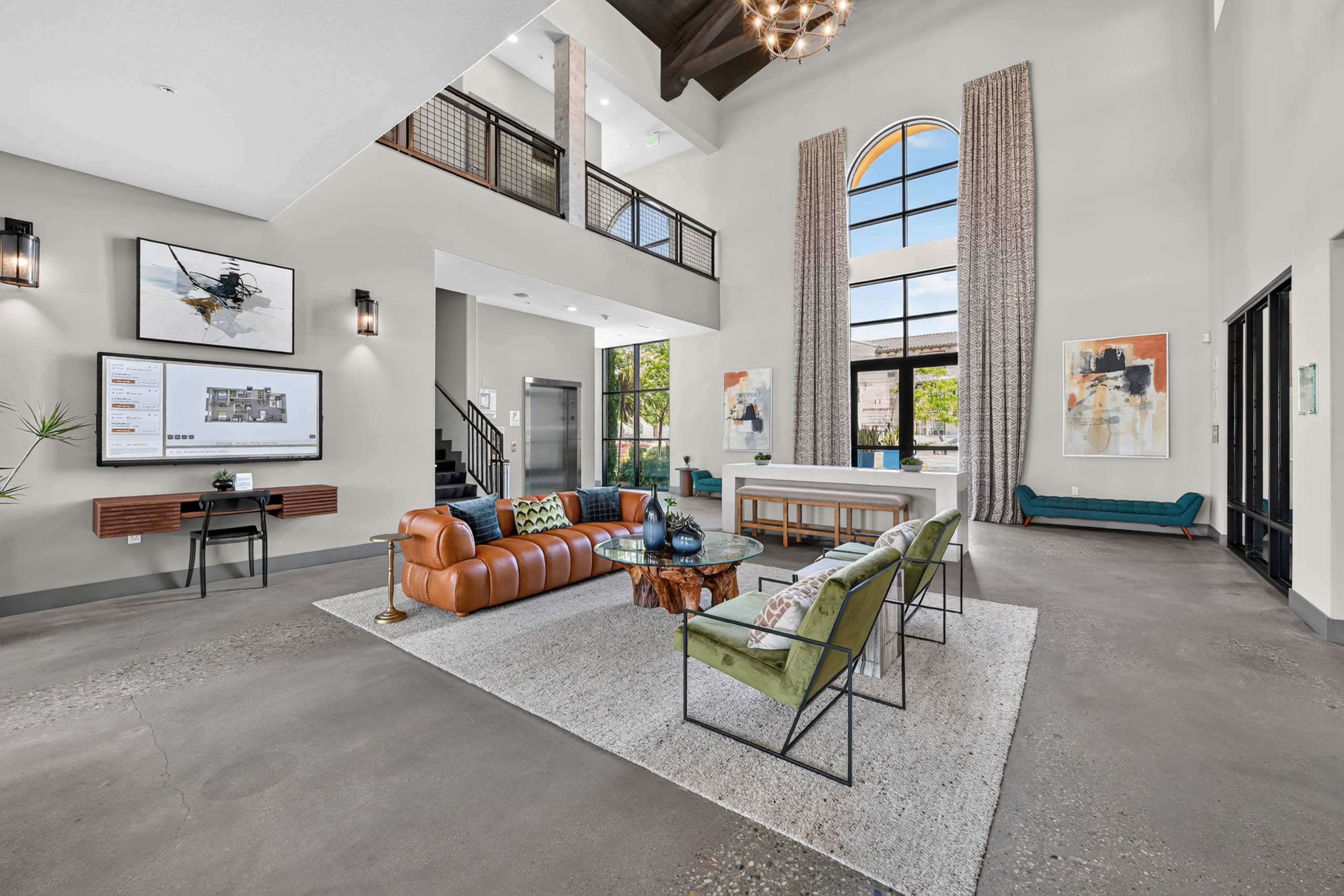 Spacious lobby at AMLI Camarillo apartments with leather sofa, green lounge chairs, high ceilings, tall windows and resident kiosk.