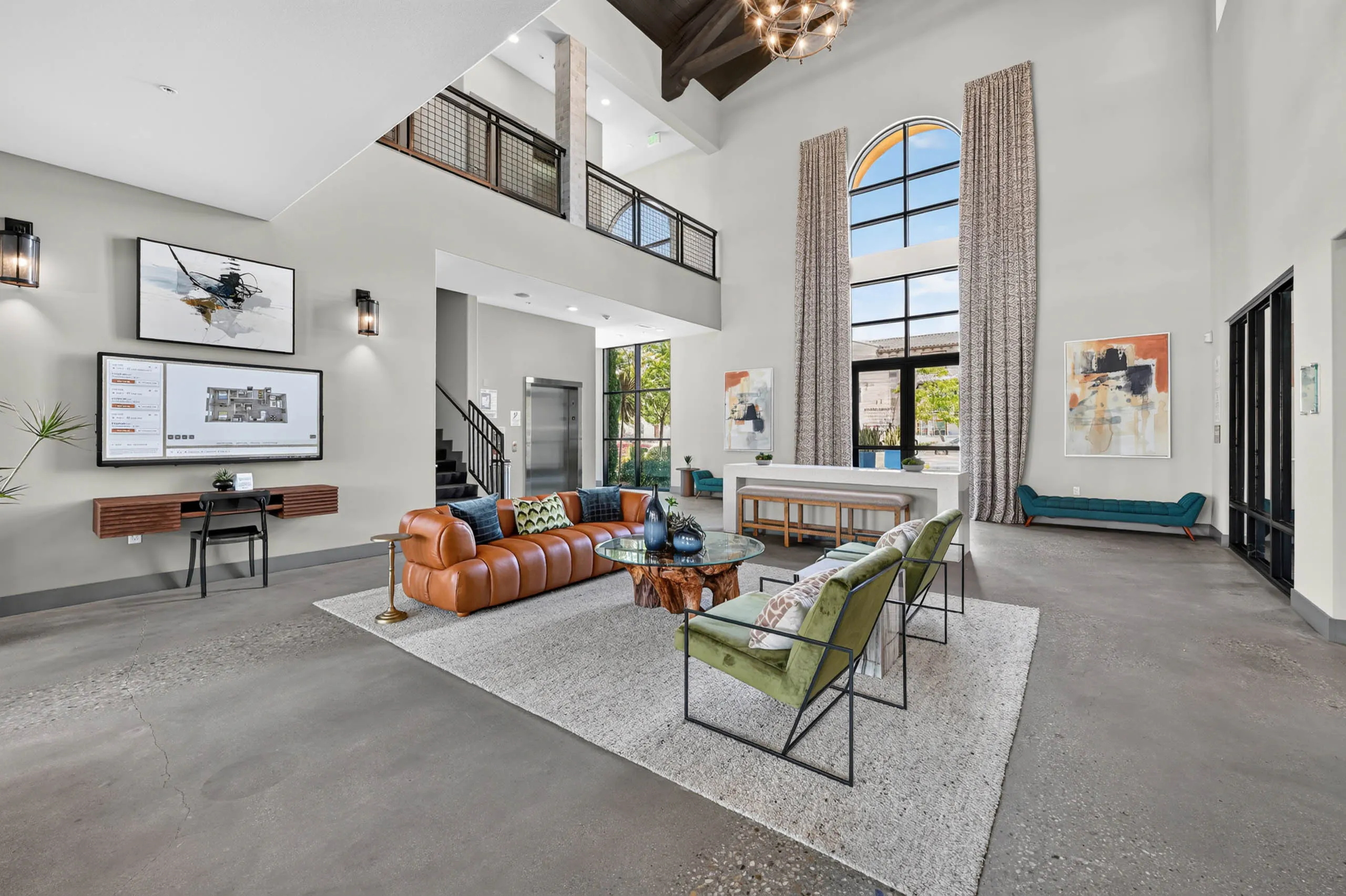 Spacious lobby at AMLI Camarillo apartments with leather sofa, green lounge chairs, high ceilings, tall windows and resident kiosk.