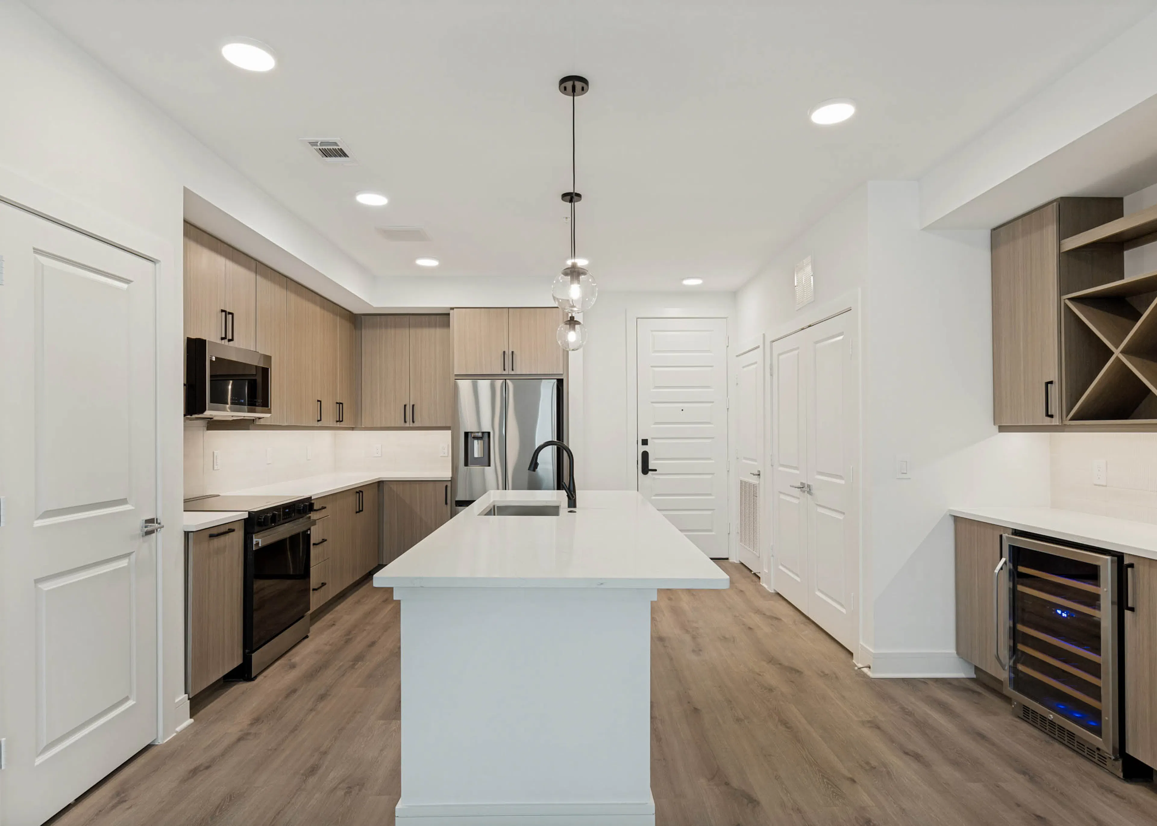 Spacious kitchen with large island, stainless steel appliances, wine refrigerator, built-in storage, pendant lighting, and wood flooring.
