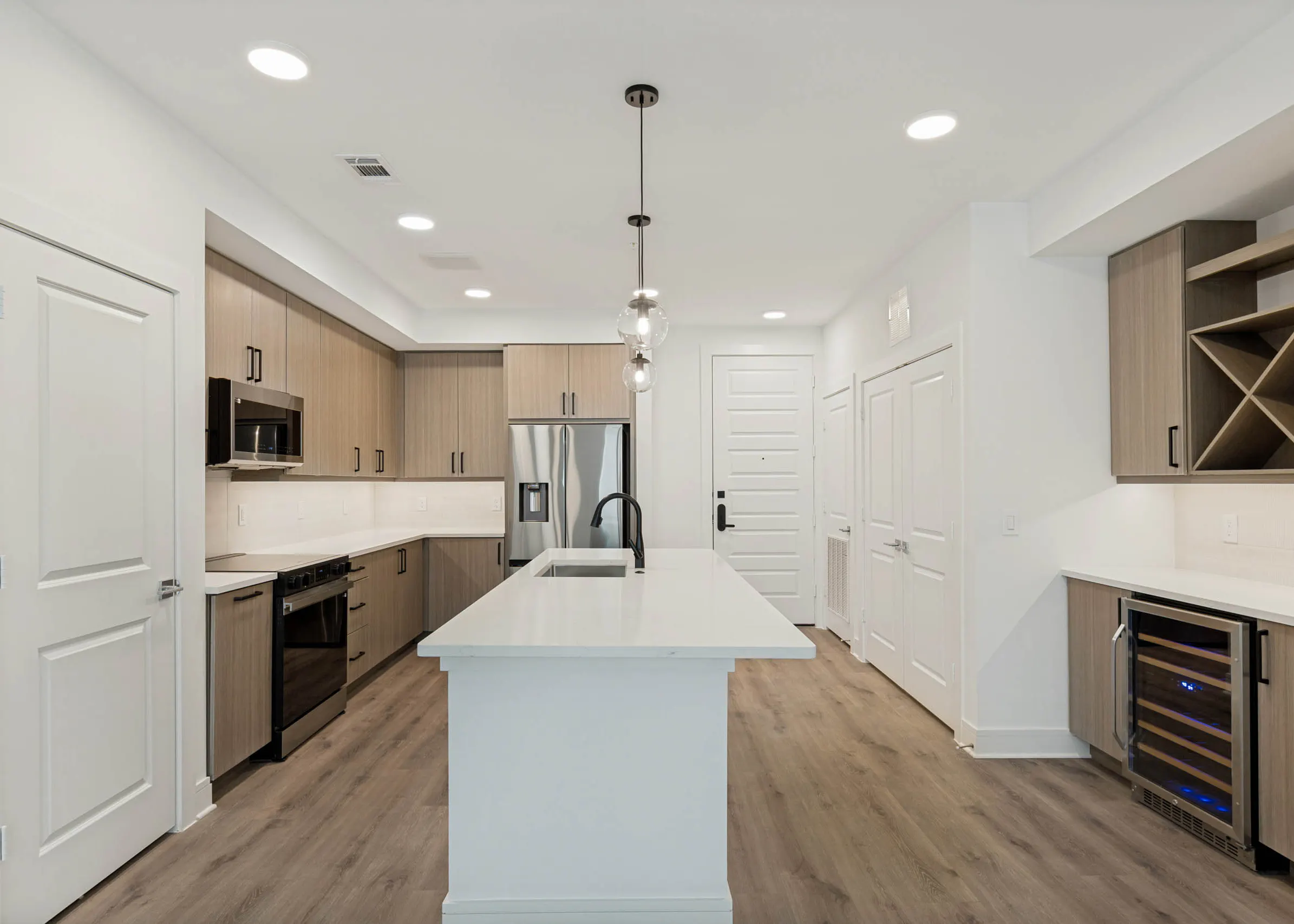 Spacious kitchen with large island, stainless steel appliances, wine refrigerator, built-in storage, pendant lighting, and wood flooring.