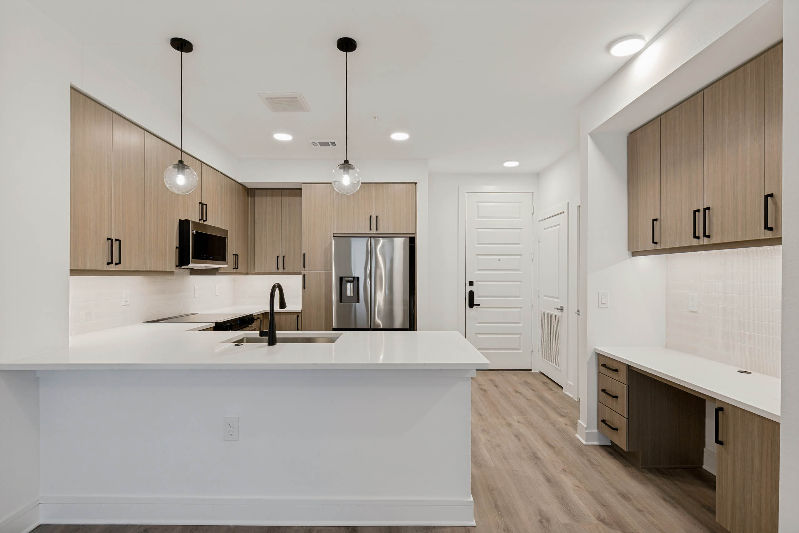 Contemporary kitchen with quartz countertops, stainless steel appliances, pendant lighting, built-in desk area, and wood-style cabinetry.