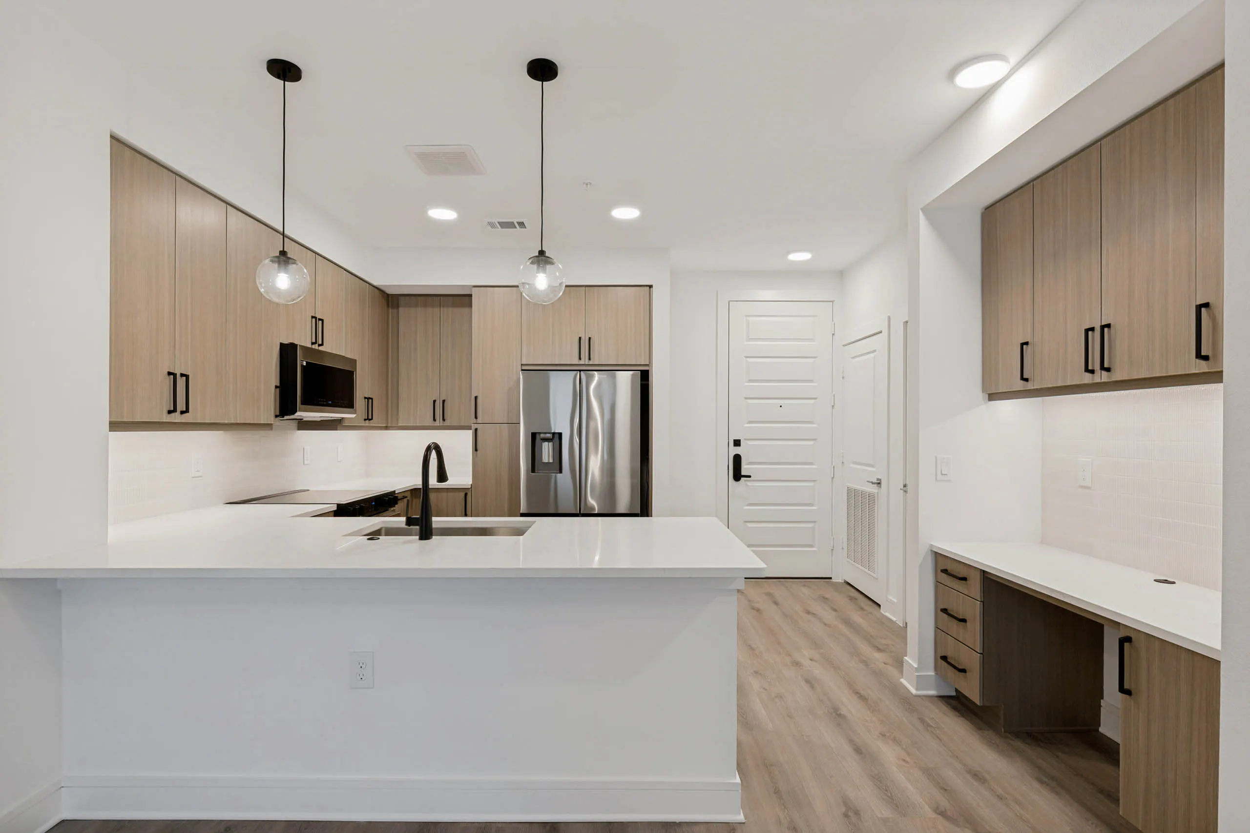 Contemporary kitchen with quartz countertops, stainless steel appliances, pendant lighting, built-in desk area, and wood-style cabinetry.
