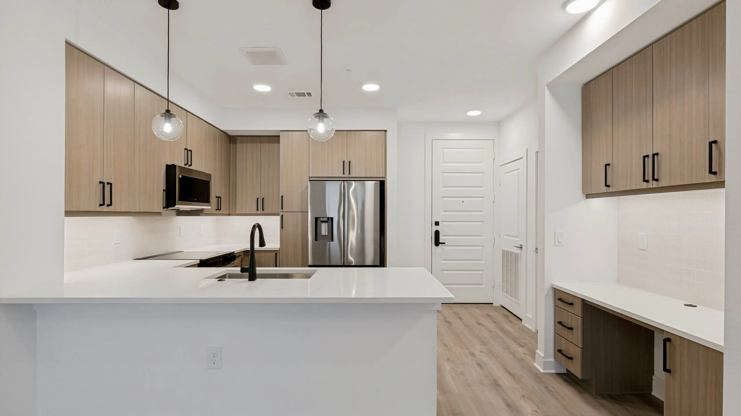 Contemporary kitchen with quartz countertops, stainless steel appliances, pendant lighting, built-in desk area, and wood-style cabinetry.