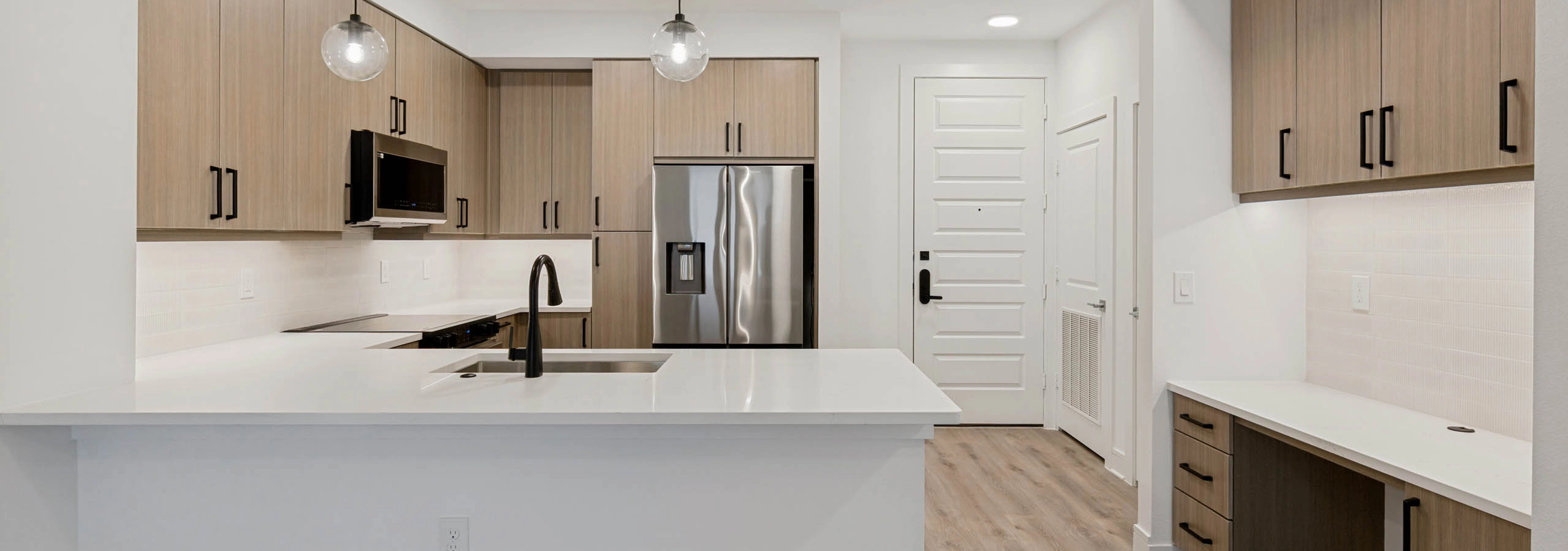Contemporary kitchen with quartz countertops, stainless steel appliances, pendant lighting, built-in desk area, and wood-style cabinetry.