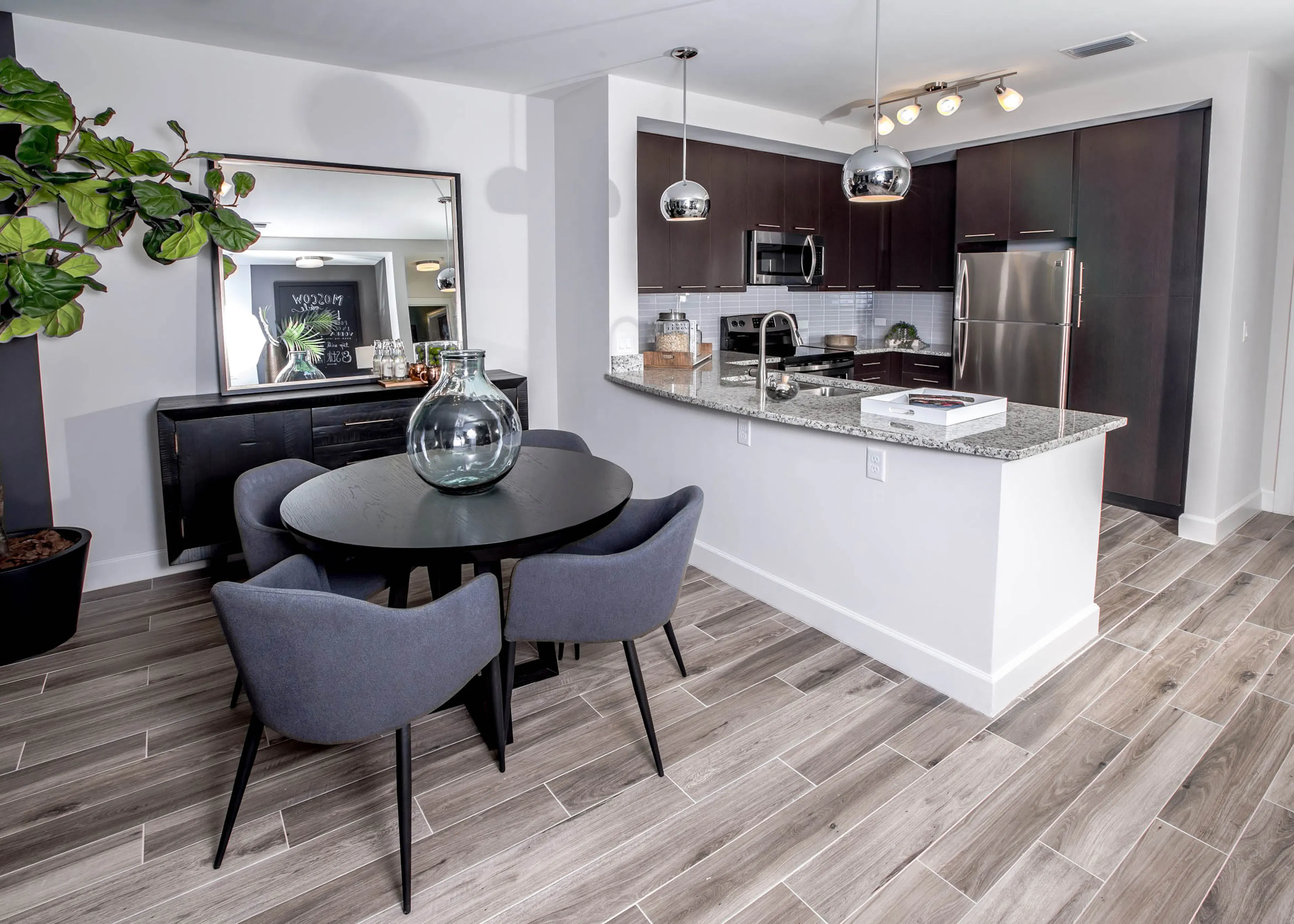 Living area at AMLI Joya apartments with contemporary decor, teal sofa with accent pillows and dining table with chairs.