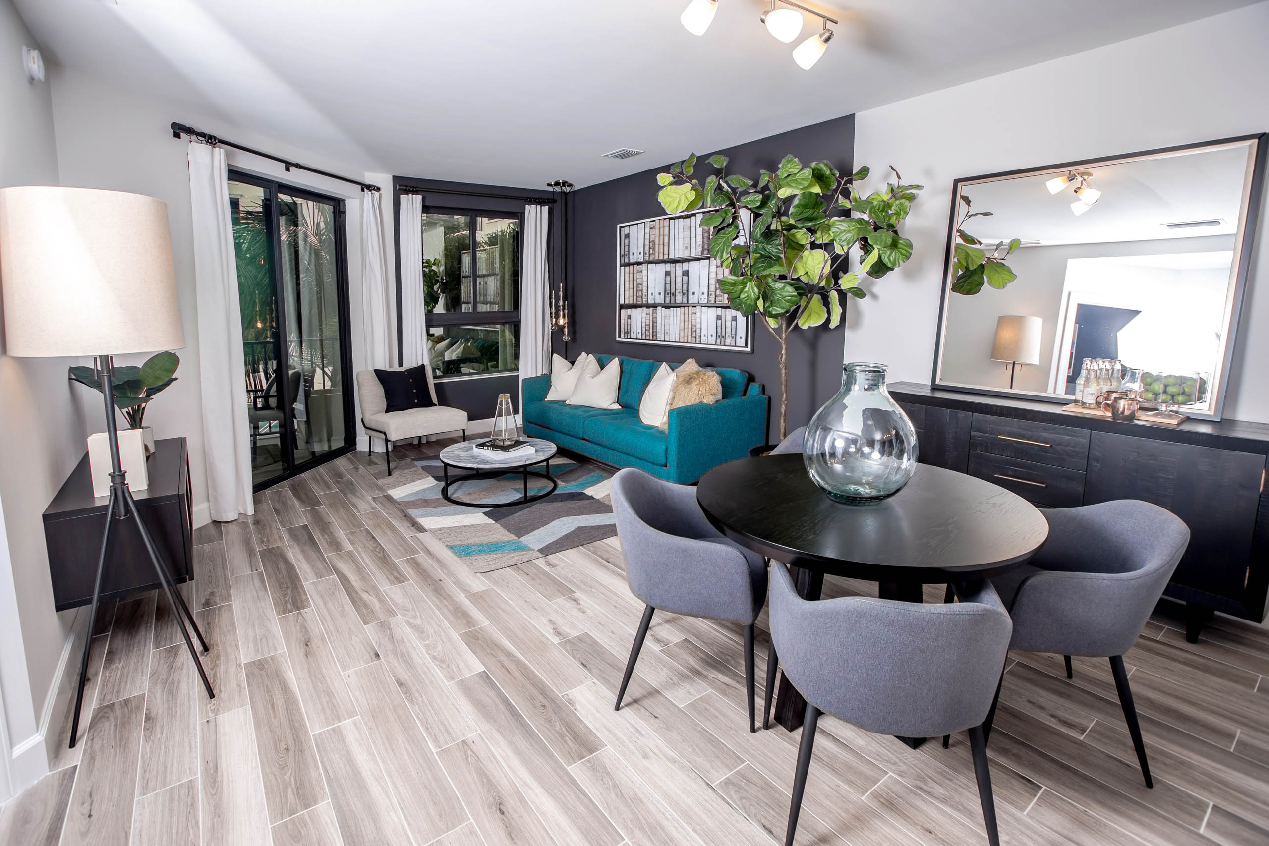 Living area at AMLI Joya apartments with contemporary decor, teal sofa with accent pillows and dining table with chairs.