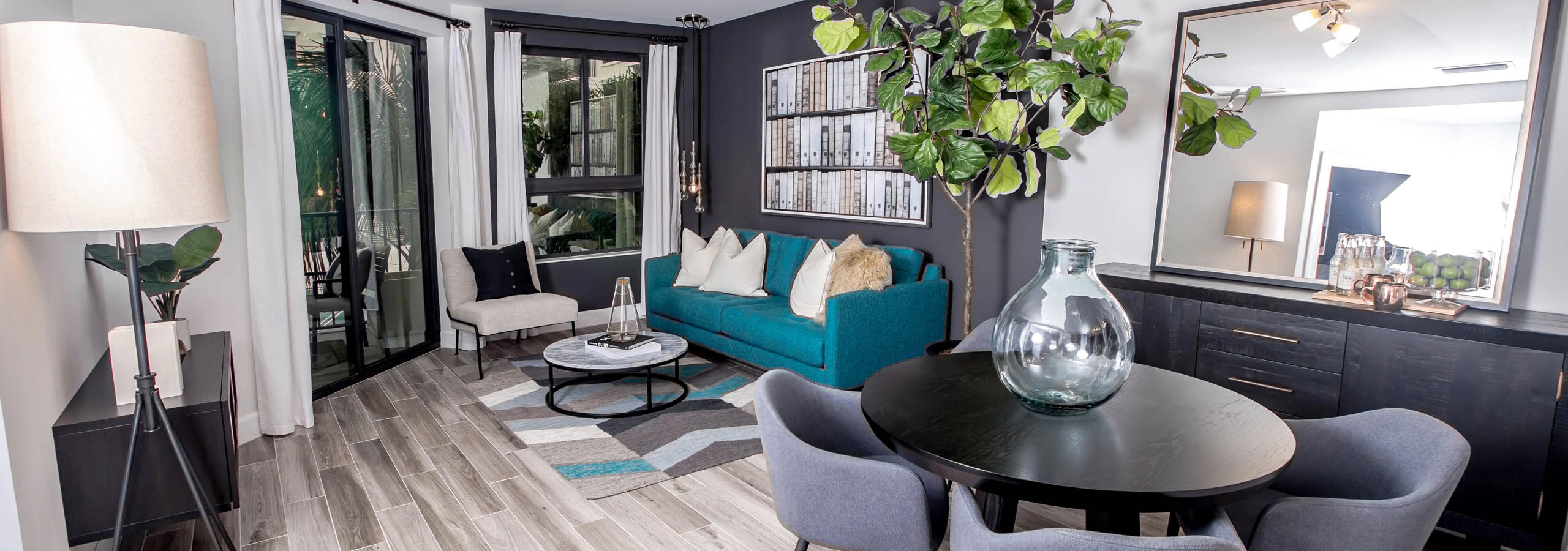 Living area at AMLI Joya apartments with contemporary decor, teal sofa with accent pillows and dining table with chairs.