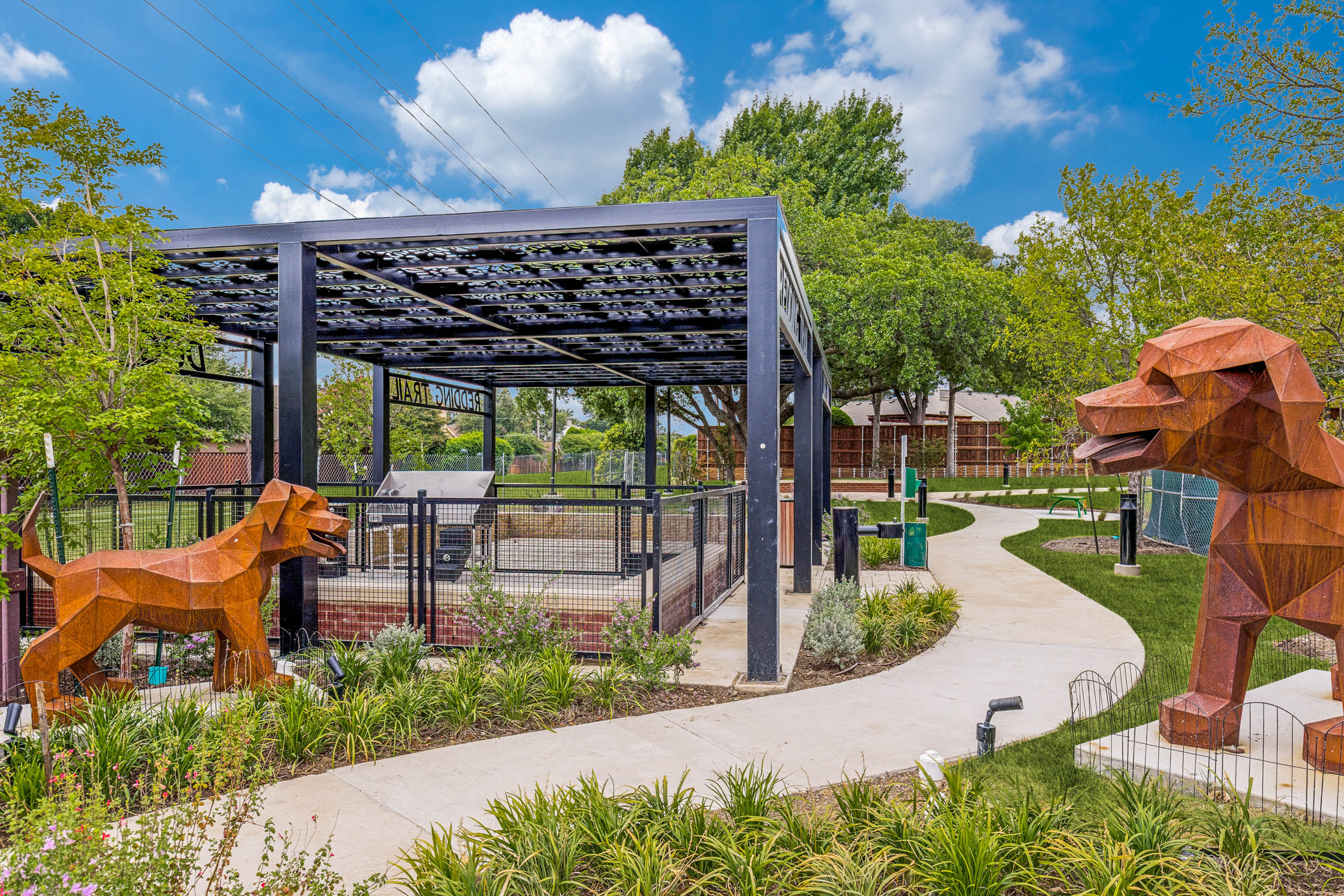 Landscaped dog park with covered pavilion, fenced play area, decorative sculptures, walking paths, and surrounding greenery at AMLI Treehouse.