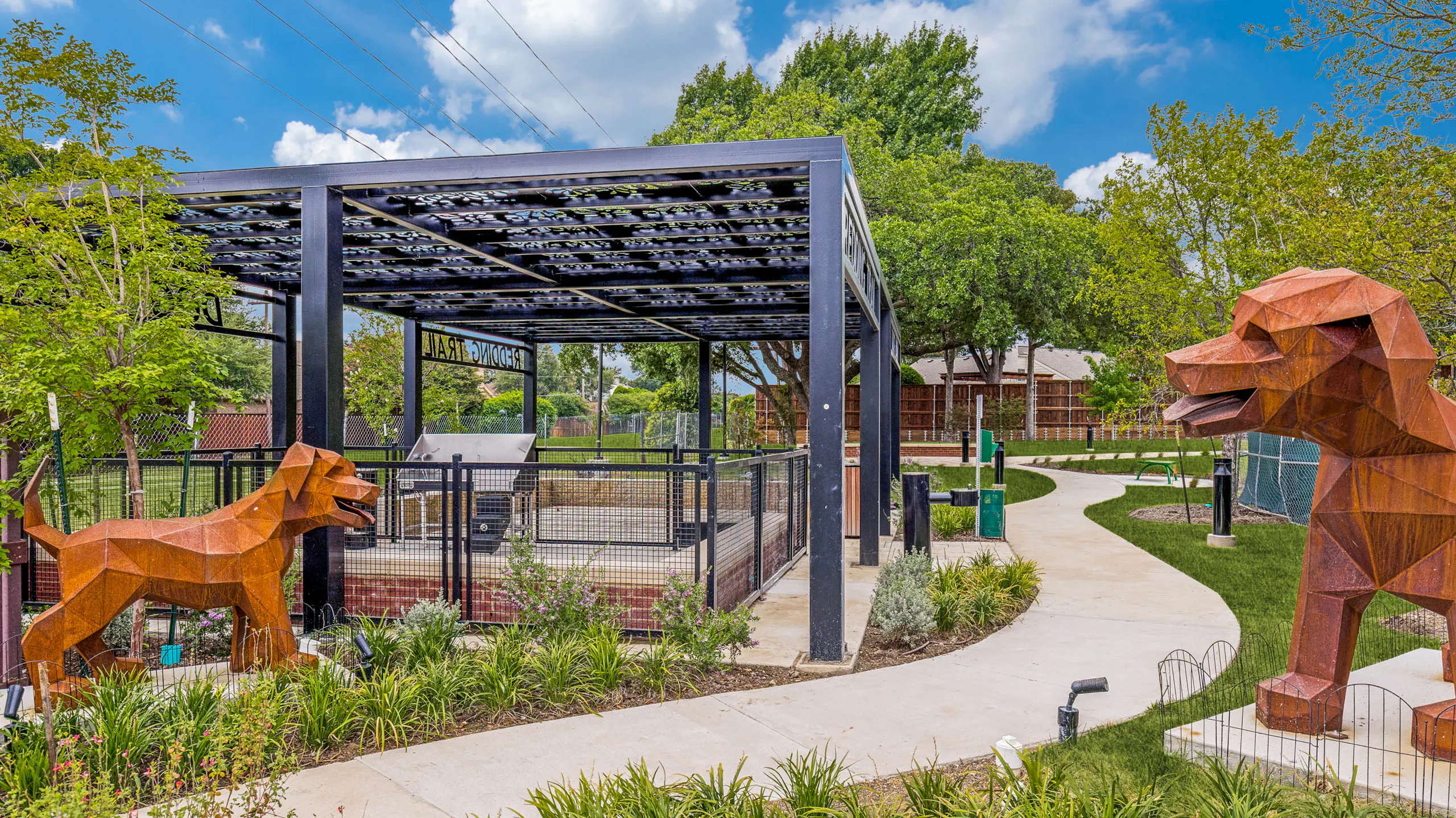 Landscaped dog park with covered pavilion, fenced play area, decorative sculptures, walking paths, and surrounding greenery at AMLI Treehouse.