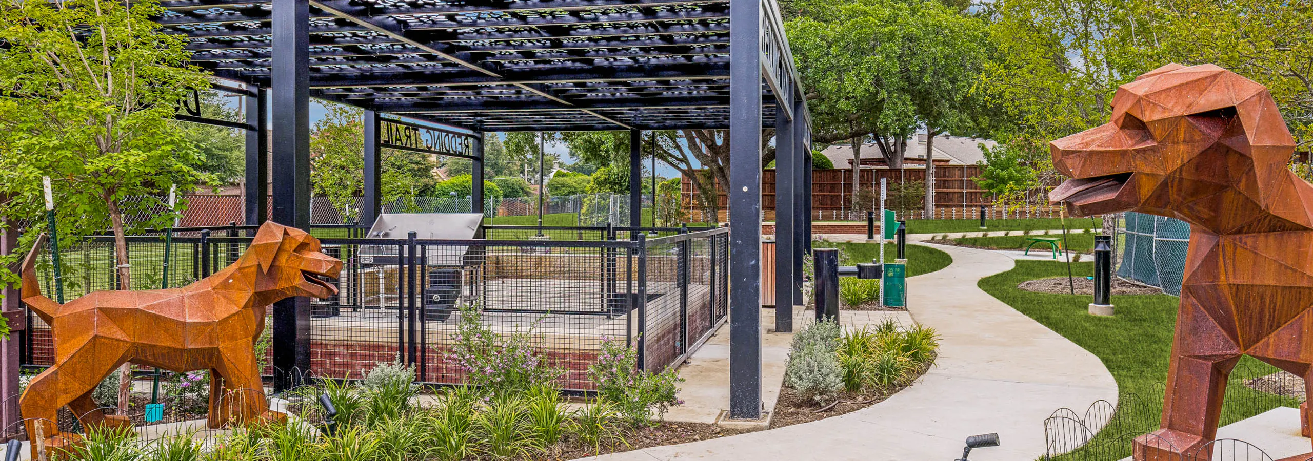 Landscaped dog park with covered pavilion, fenced play area, decorative sculptures, walking paths, and surrounding greenery at AMLI Treehouse.