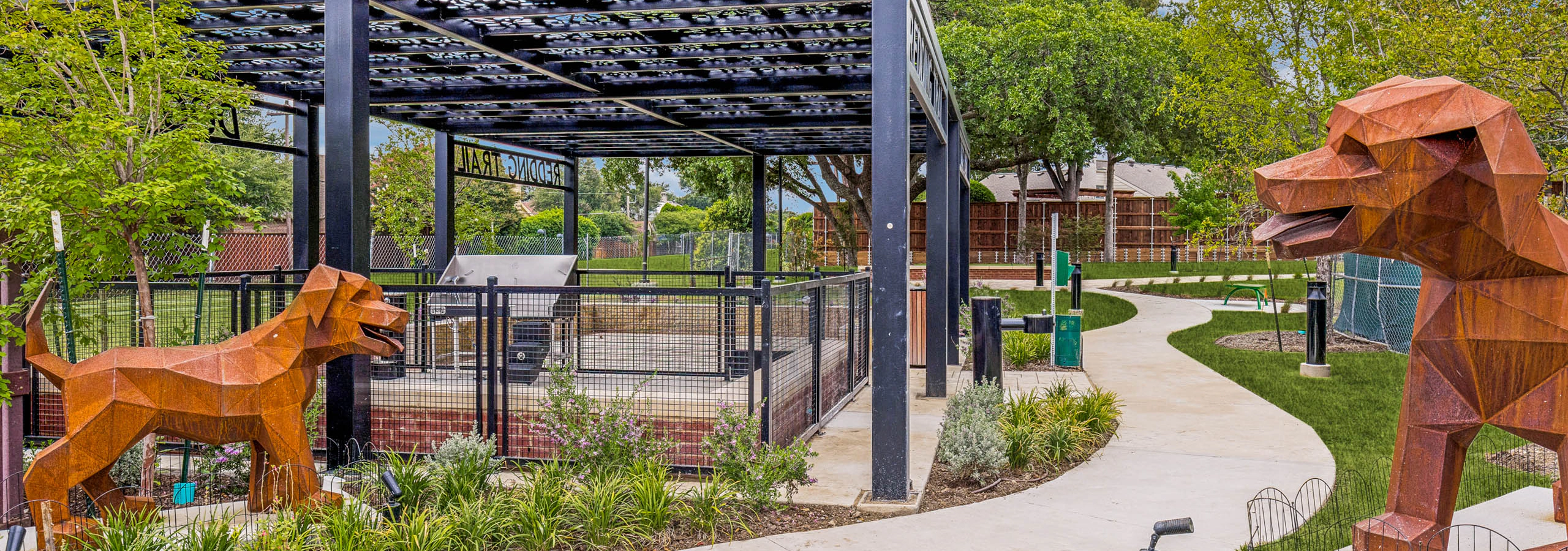 Landscaped dog park with covered pavilion, fenced play area, decorative sculptures, walking paths, and surrounding greenery at AMLI Treehouse.