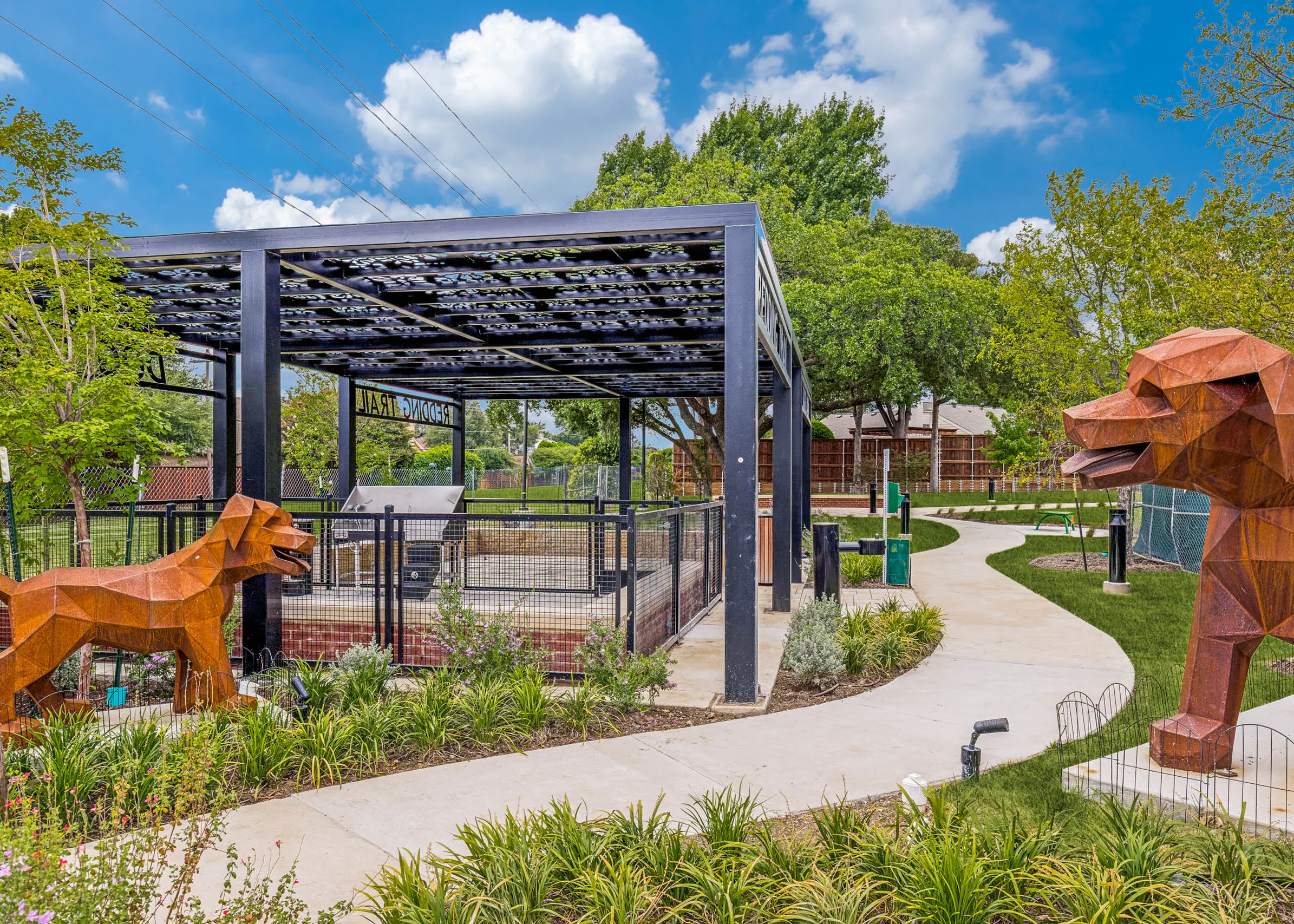 Landscaped dog park with covered pavilion, fenced play area, decorative sculptures, walking paths, and surrounding greenery at AMLI Treehouse.