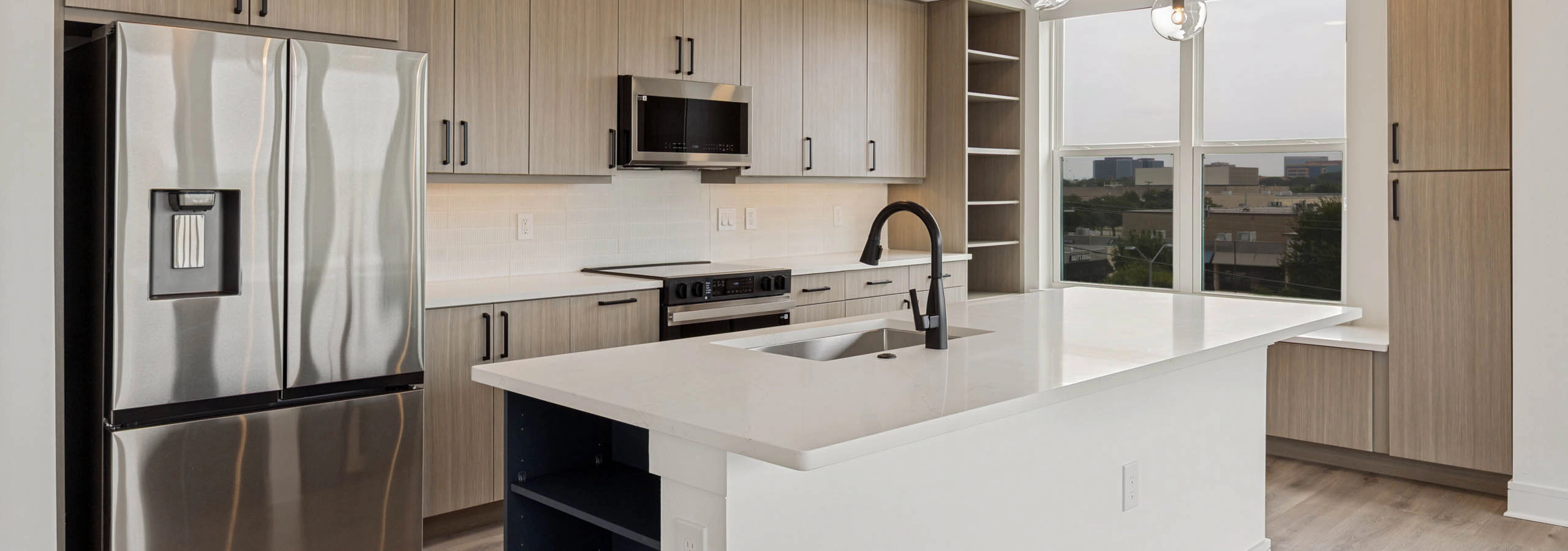 Modern kitchen with quartz island, stainless steel appliances, wood-style cabinetry, pendant lighting, open shelving, and large windows.
