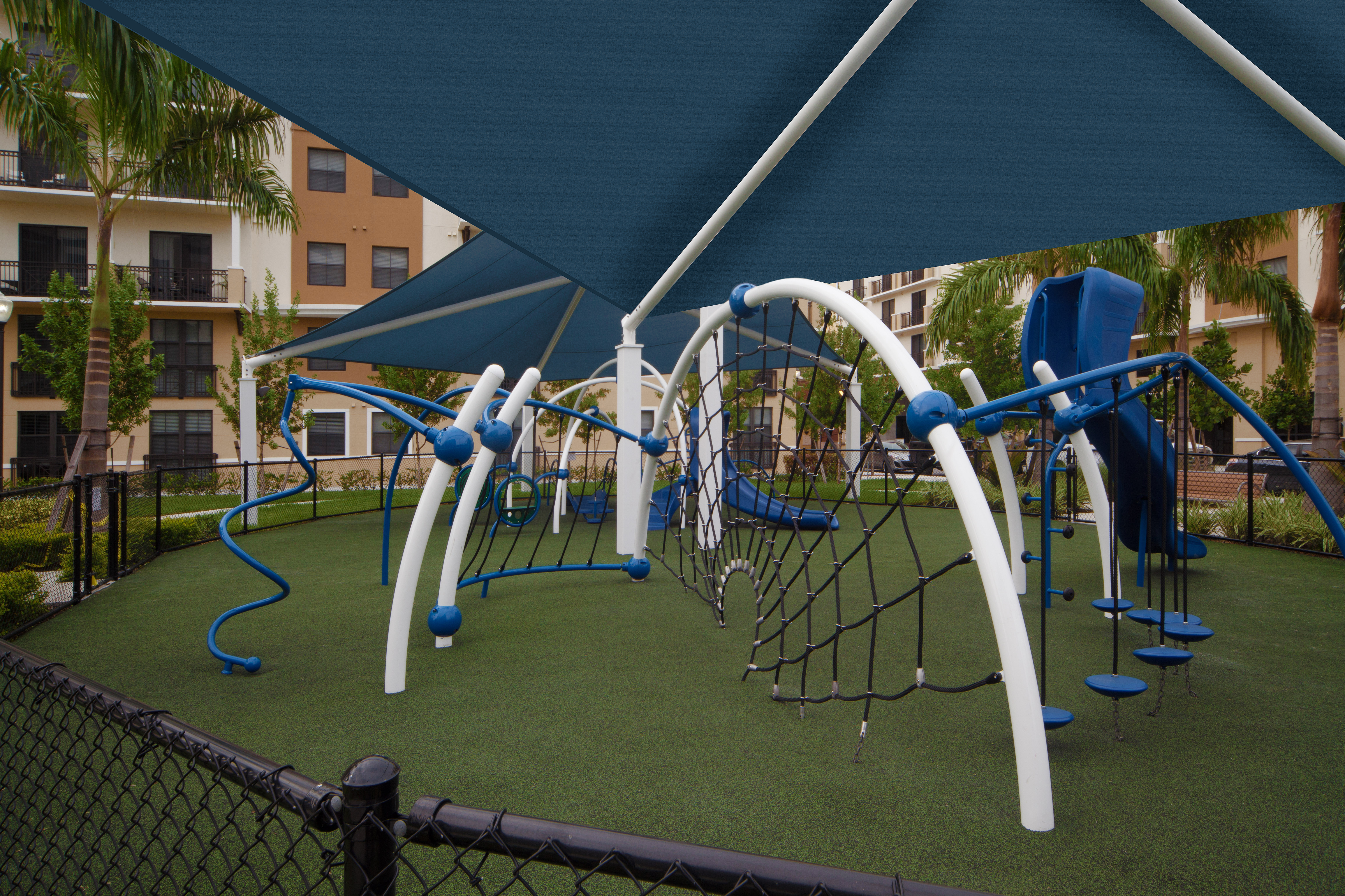 Modern Children’s covered playground at AMLI Dadeland with blue and white recreational equipment on faux grass foundation