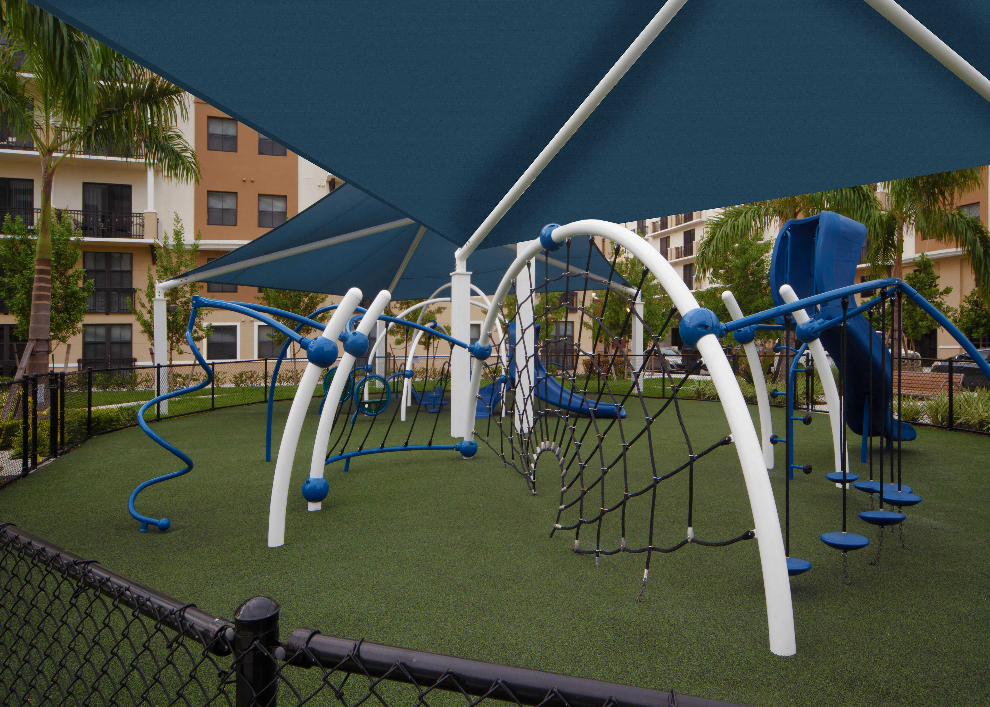 Modern Children’s covered playground at AMLI Dadeland with blue and white recreational equipment on faux grass foundation