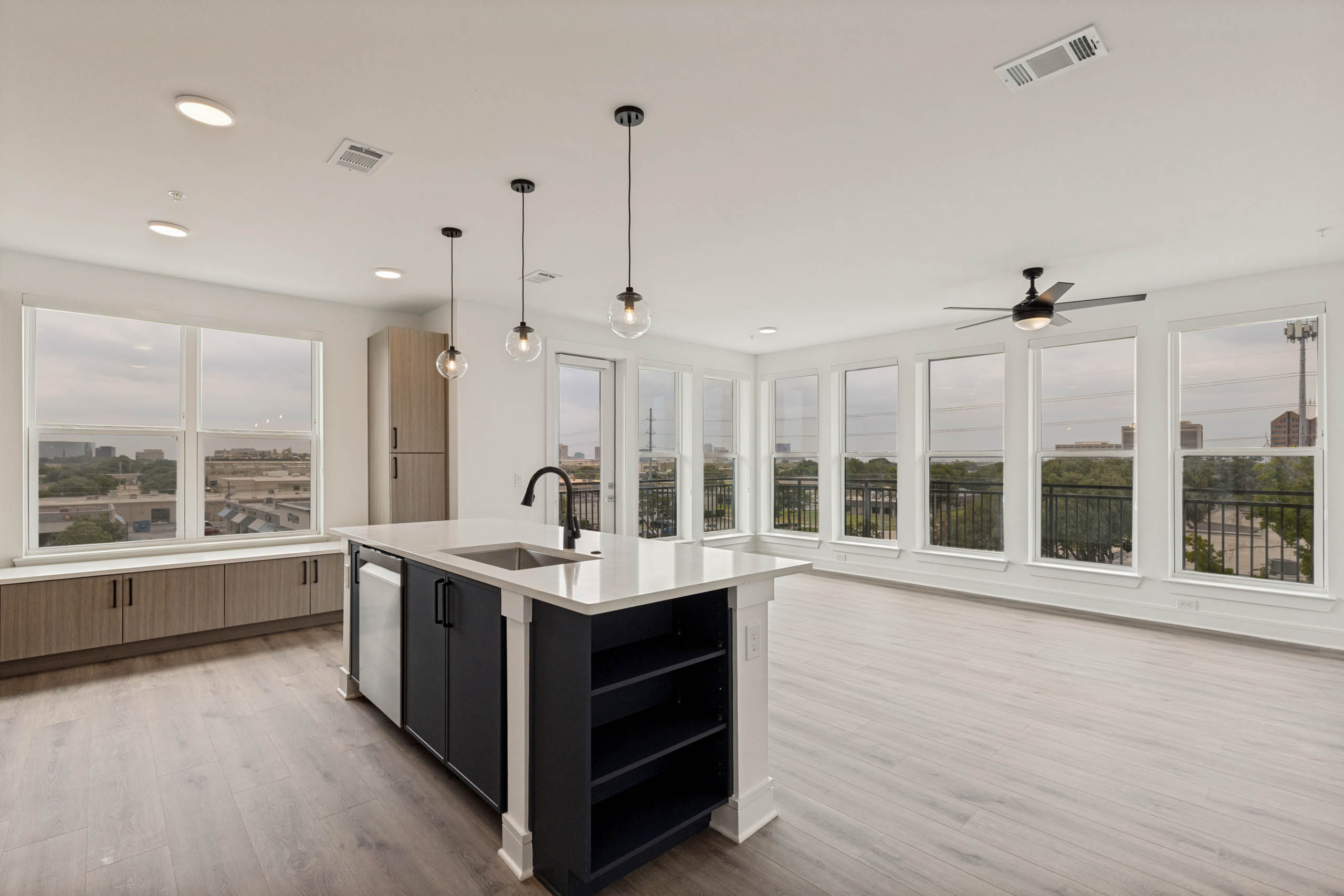 Open-concept apartment home with kitchen island, pendant lighting, expansive windows, built-in storage, balcony access, and abundant natural light.