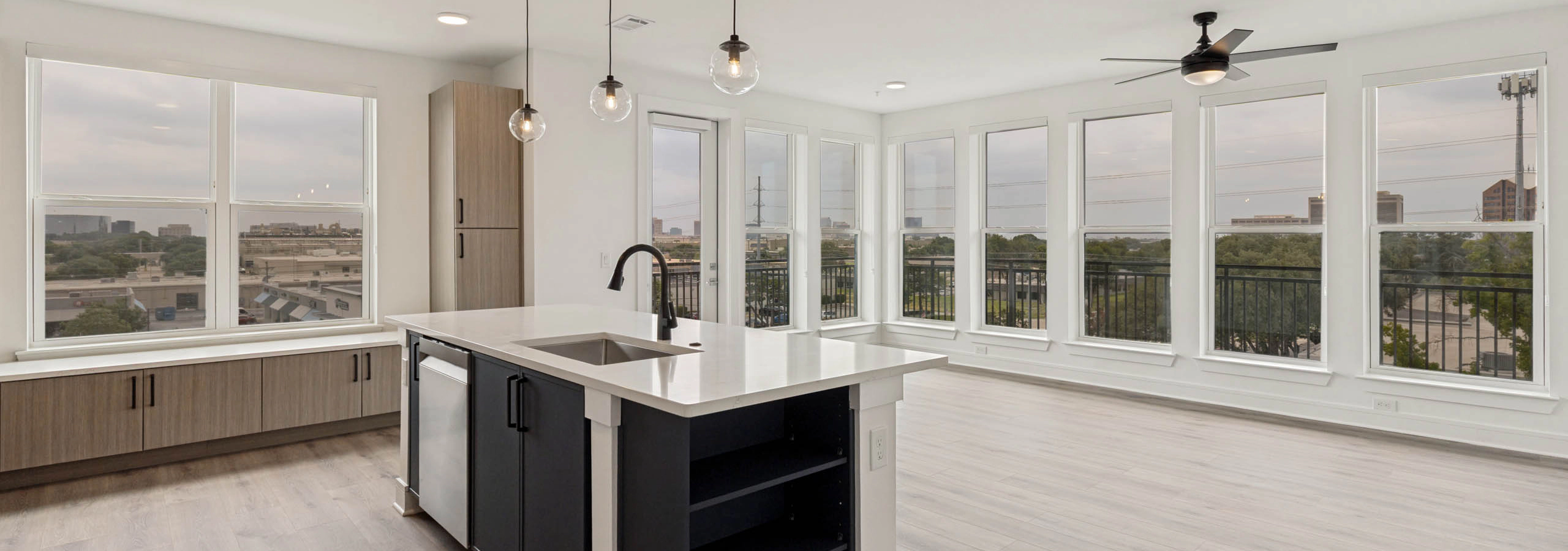Open-concept apartment home with kitchen island, pendant lighting, expansive windows, built-in storage, balcony access, and abundant natural light.