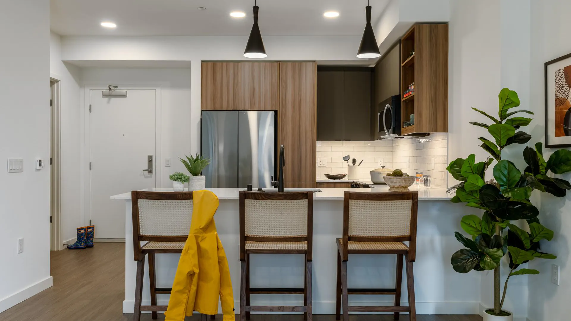 A sleek luxury apartment kitchen with stainless steel appliances and wooden cabinets and a breakfast nook with three stools