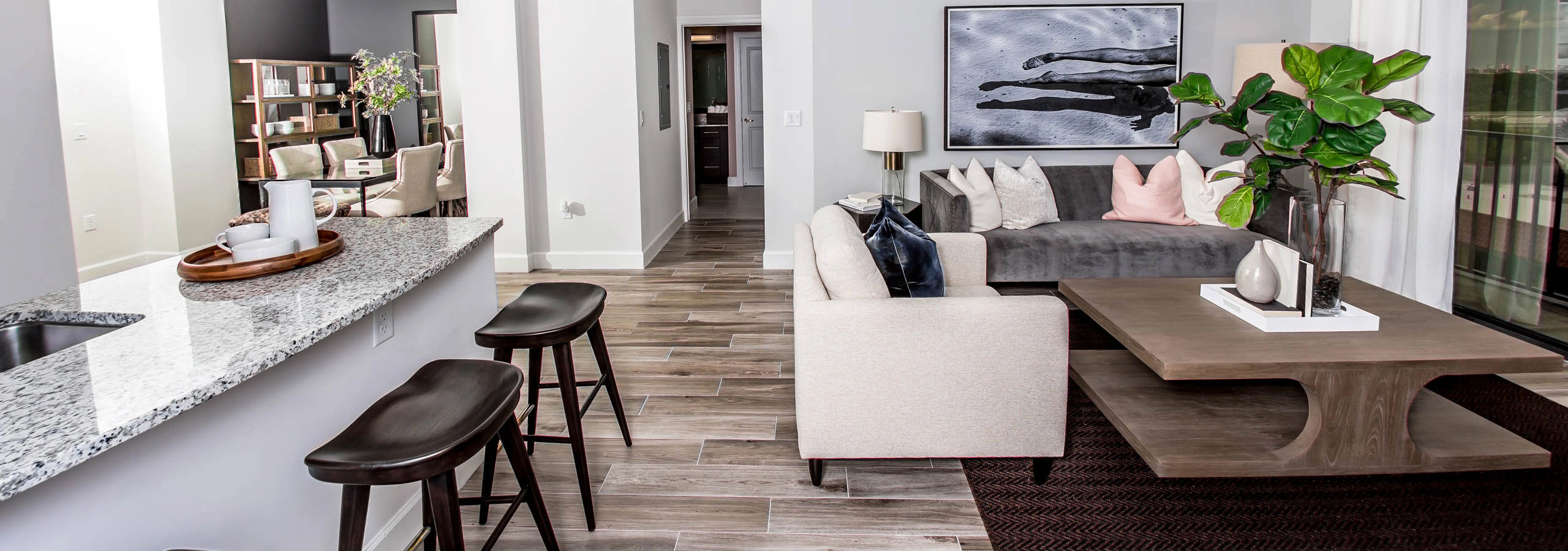 An apartment living room at AMLI Joya with cool neutral colors, a couch and coffee table and kitchen island with stools.