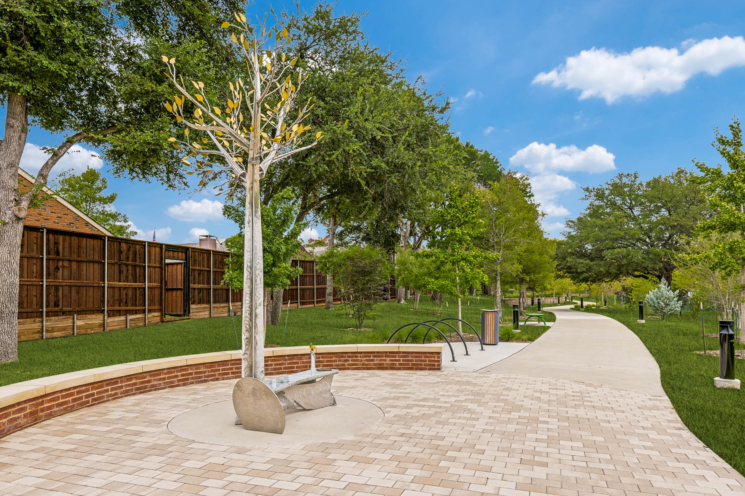 Connected community trail featuring a decorative tree sculpture, paved seating area, landscaped greenery, pathway lighting, and open green space at AMLI Treehouse.
