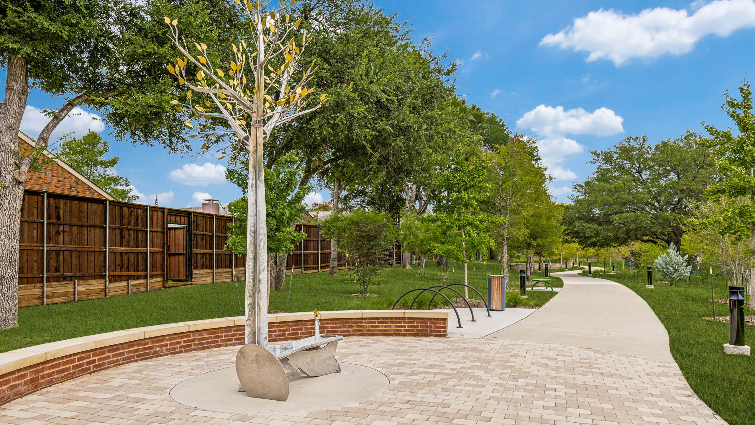 Park-like community trail featuring a decorative tree sculpture, paved seating area, landscaped greenery, pathway lighting, and open green space at AMLI Treehouse.