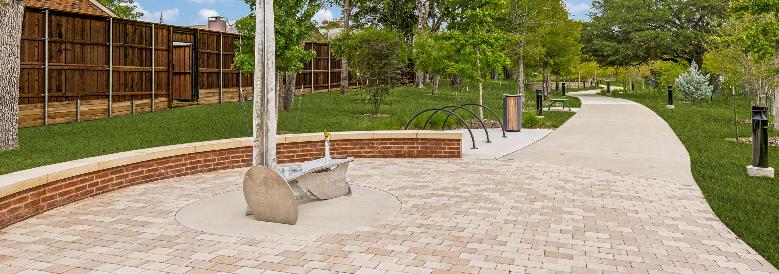Connected community trail featuring a decorative tree sculpture, paved seating area, landscaped greenery, pathway lighting, and open green space at AMLI Treehouse.